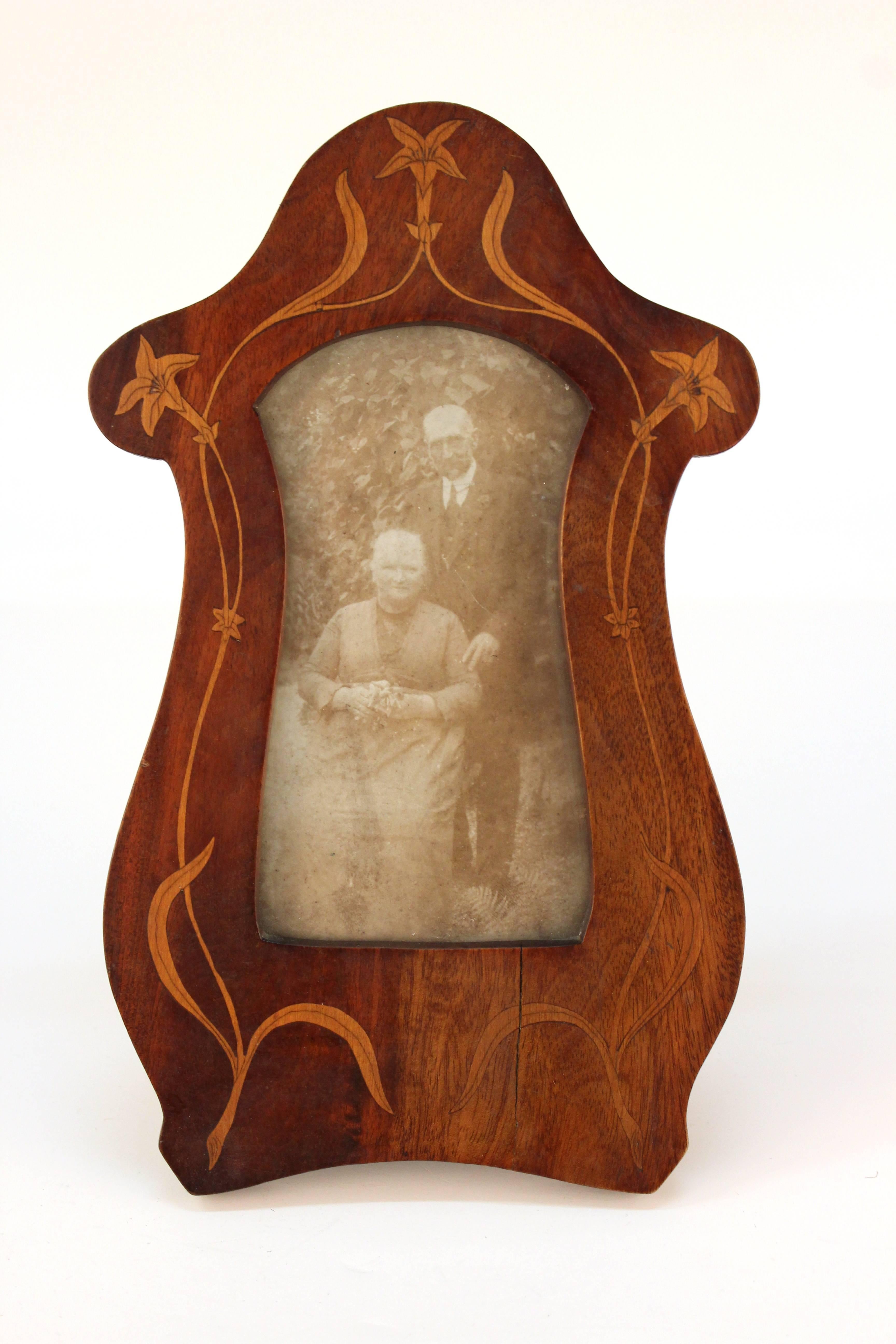 An Art Nouveau picture frame. Organically shaped with floral accents. The frame includes an original black and white photo of an elderly couple. Despite some wear to the frame and fading to the photograph the item remains in overall good vintage