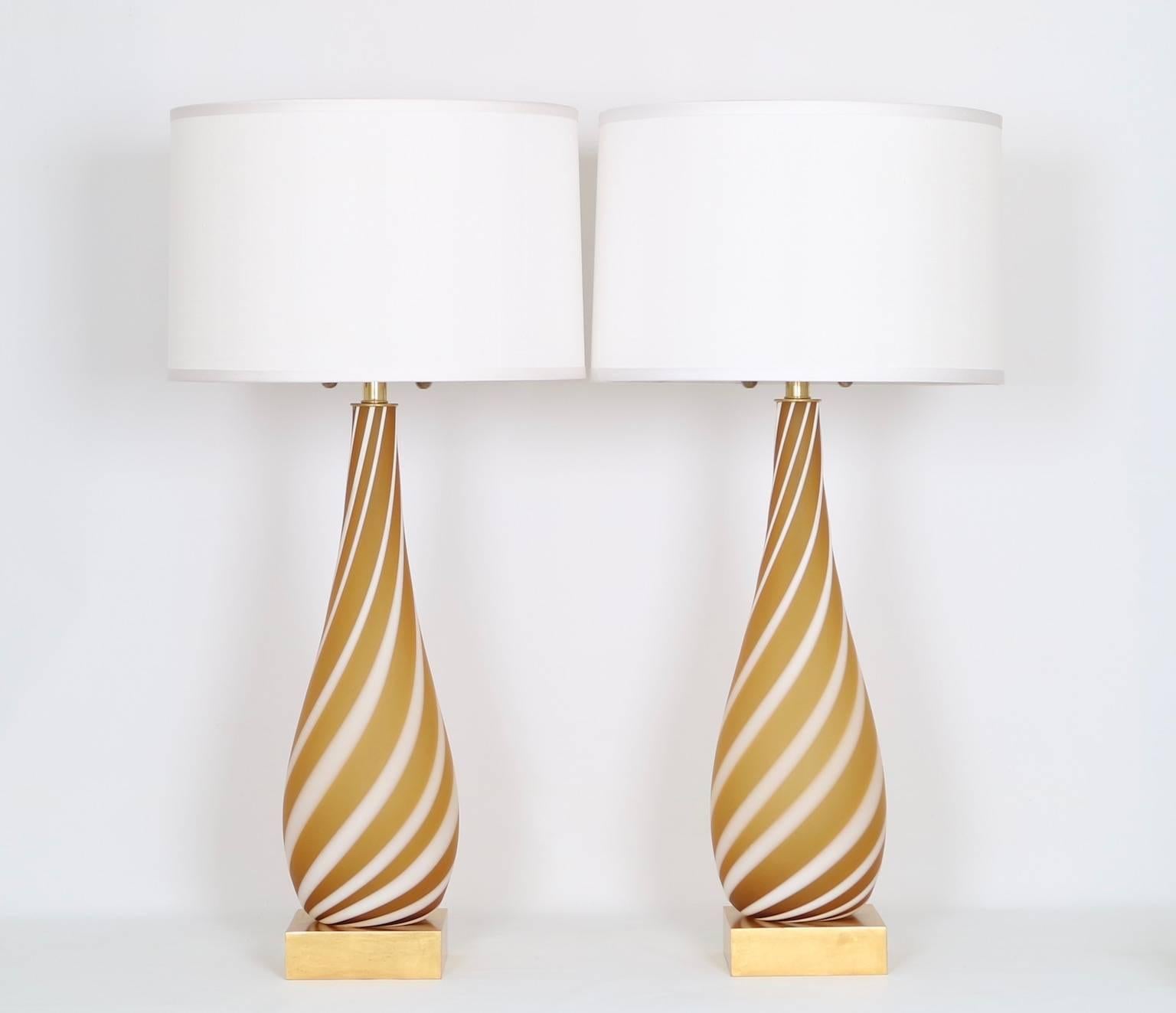 Pair of Mid-Century Modern Murano glass lamps in butterscotch with a white ribbon swirl and mounted on a gilded wooden base. The noted height is to the finial,the height to the top of the glass body is 23.5 in (60 cm). Fully restored with all new