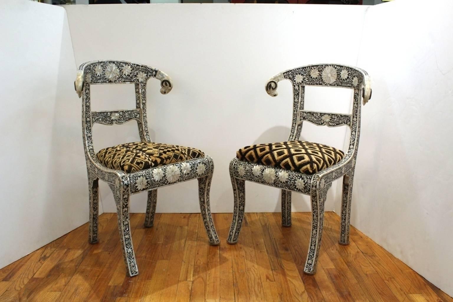 Pair of Klismos chairs inlaid with bone and mother-of-pearl arranged in elaborate floral designs. Includes a pair of detailed ram heads on each end of the chair back. Despite some small chips and missing tiles to the inlay, the chairs remain in
