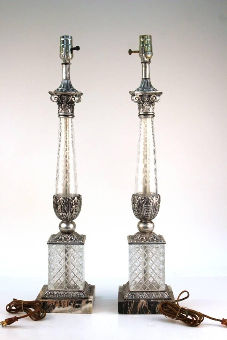 This pair of glass lamps features neoclassical Corinthian columns and a marble base. Each lamp features cut glass lower stems. In good vintage condition, consistent with age and use. 110799.