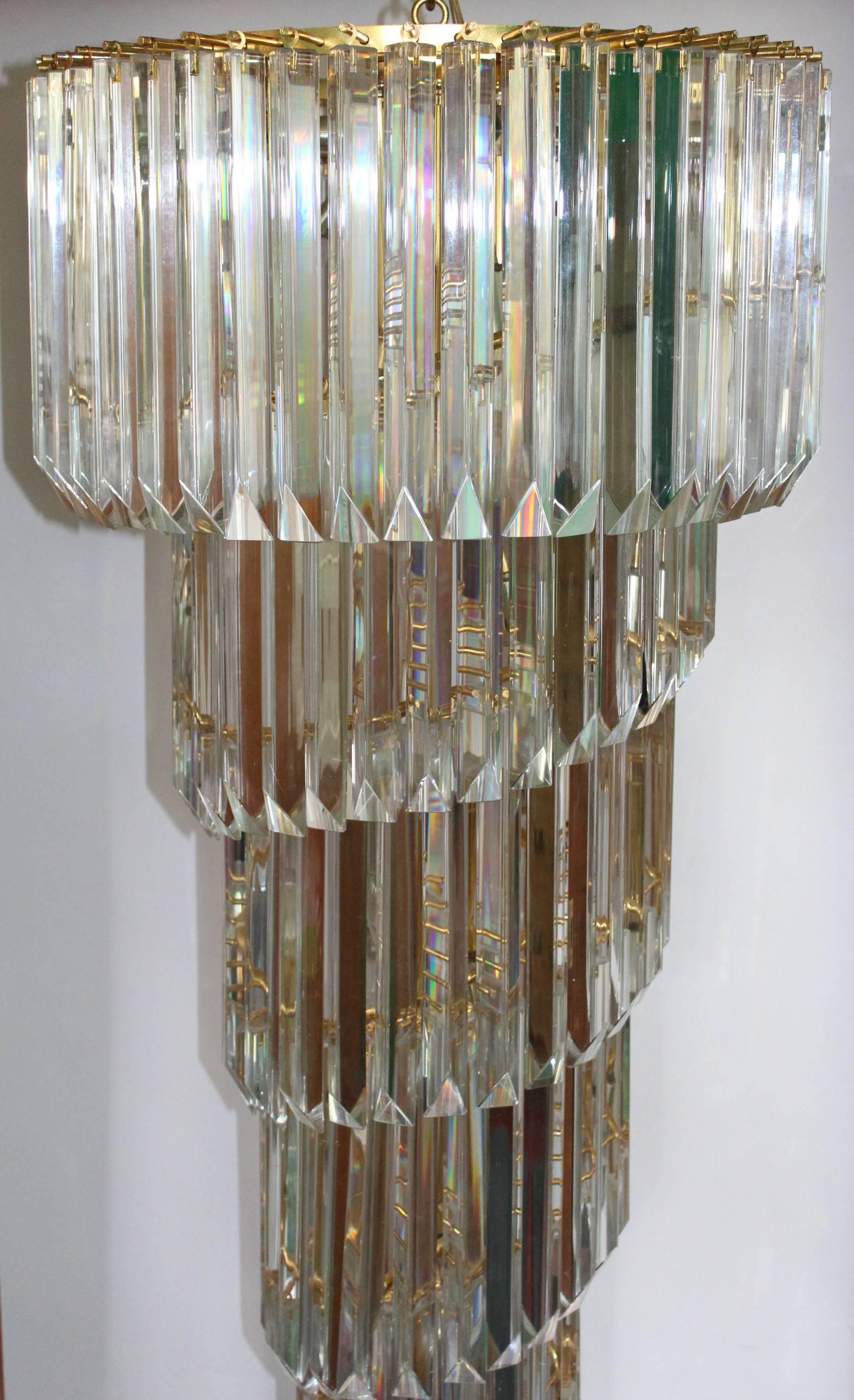 This chandelier in the manner of Camer with cascading crystal prisms includes a ceiling plate. Each crystal measures 11 inches long and the diameter across the widest point of the chandelier measures 21 inches. It remains in very good condition. One