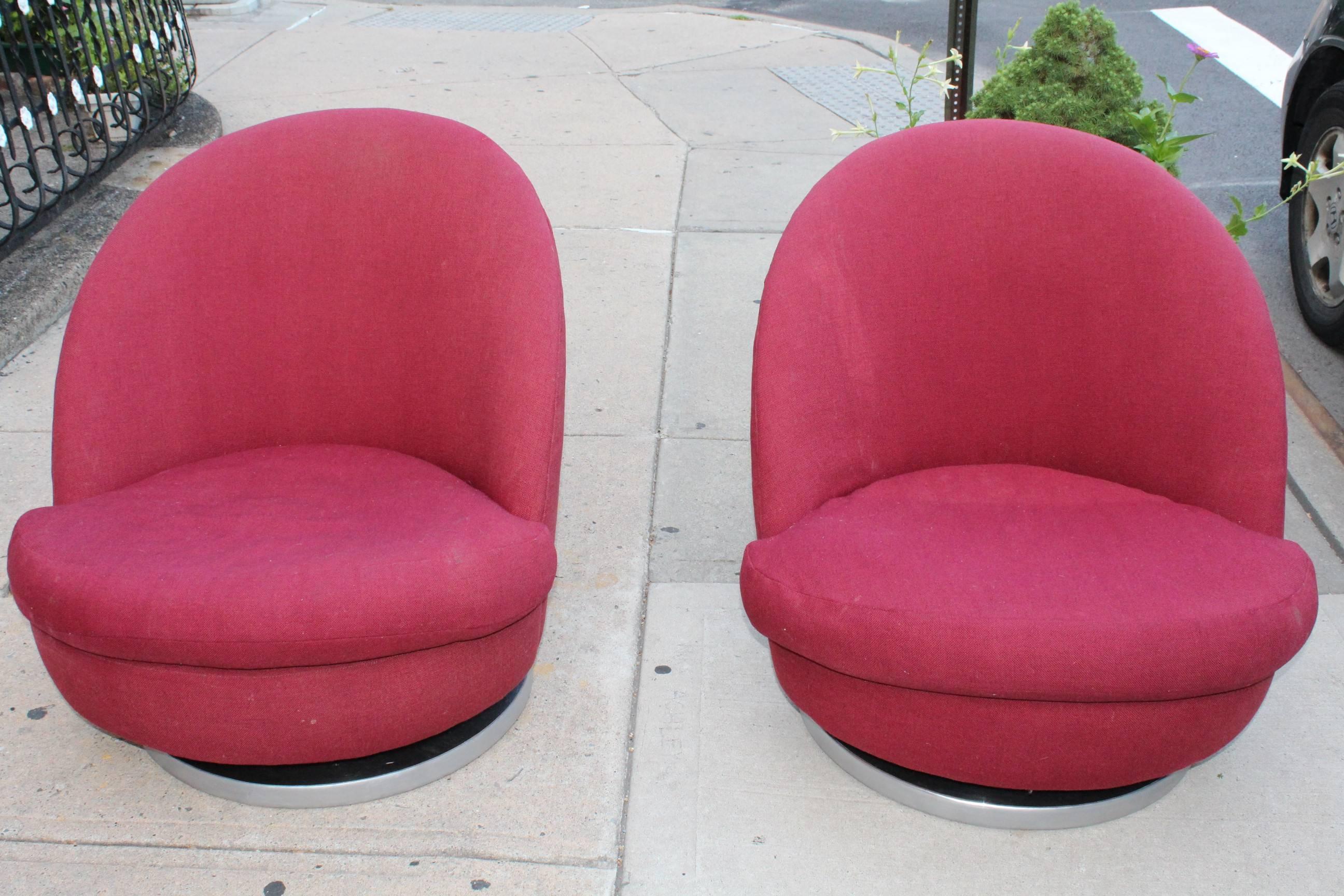 This pair of red lounge chairs by Milo Baughman for Thayer Coggin are mounted on chrome bases and date from the 1970s. Each is in vintage condition, with staining to the upholstery. There is a rip in the lining beneath the cushion of one seat.