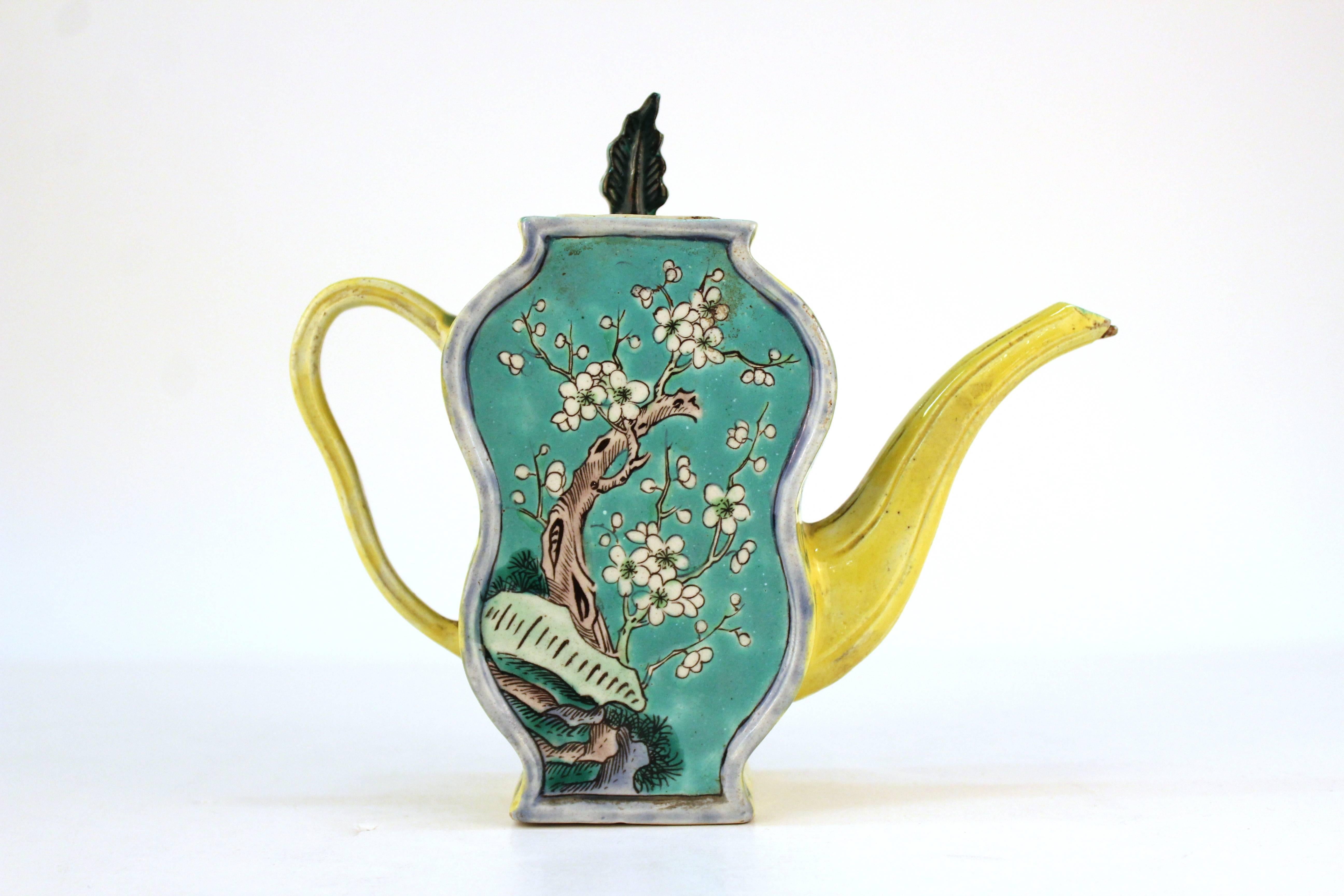 Chinese porcelain teapot with a warrior and florals against a vivid aqua and bright yellow background and topped with a tea leaf. Marked China on the bottom. Chips to the spout and lid but in overall good condition.