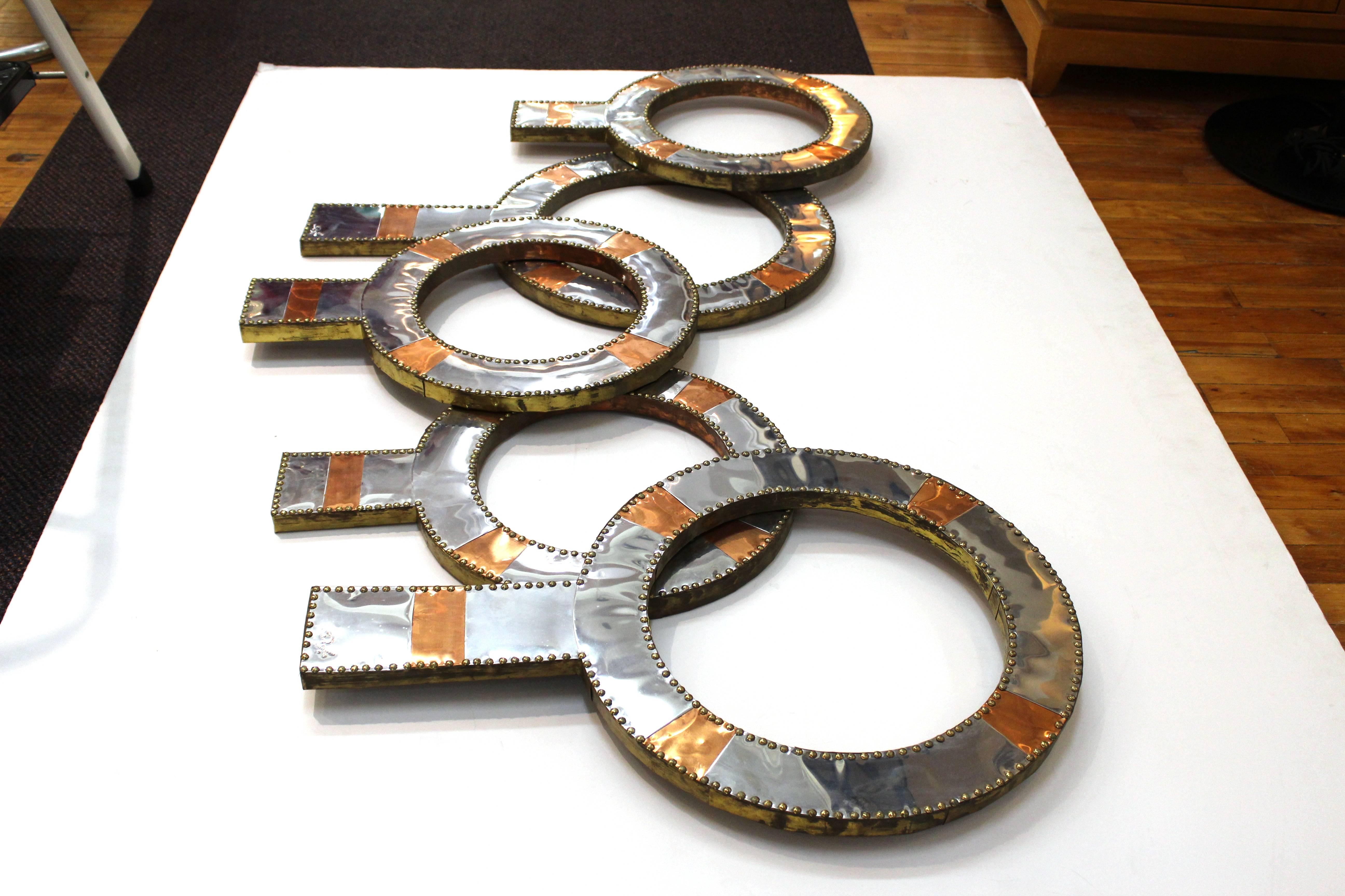 A wall sculpture by Don Freedman in the form of five overlapping rings of various sizes with two tones of metal. Initialed by the artist at the bottom of two rings.
