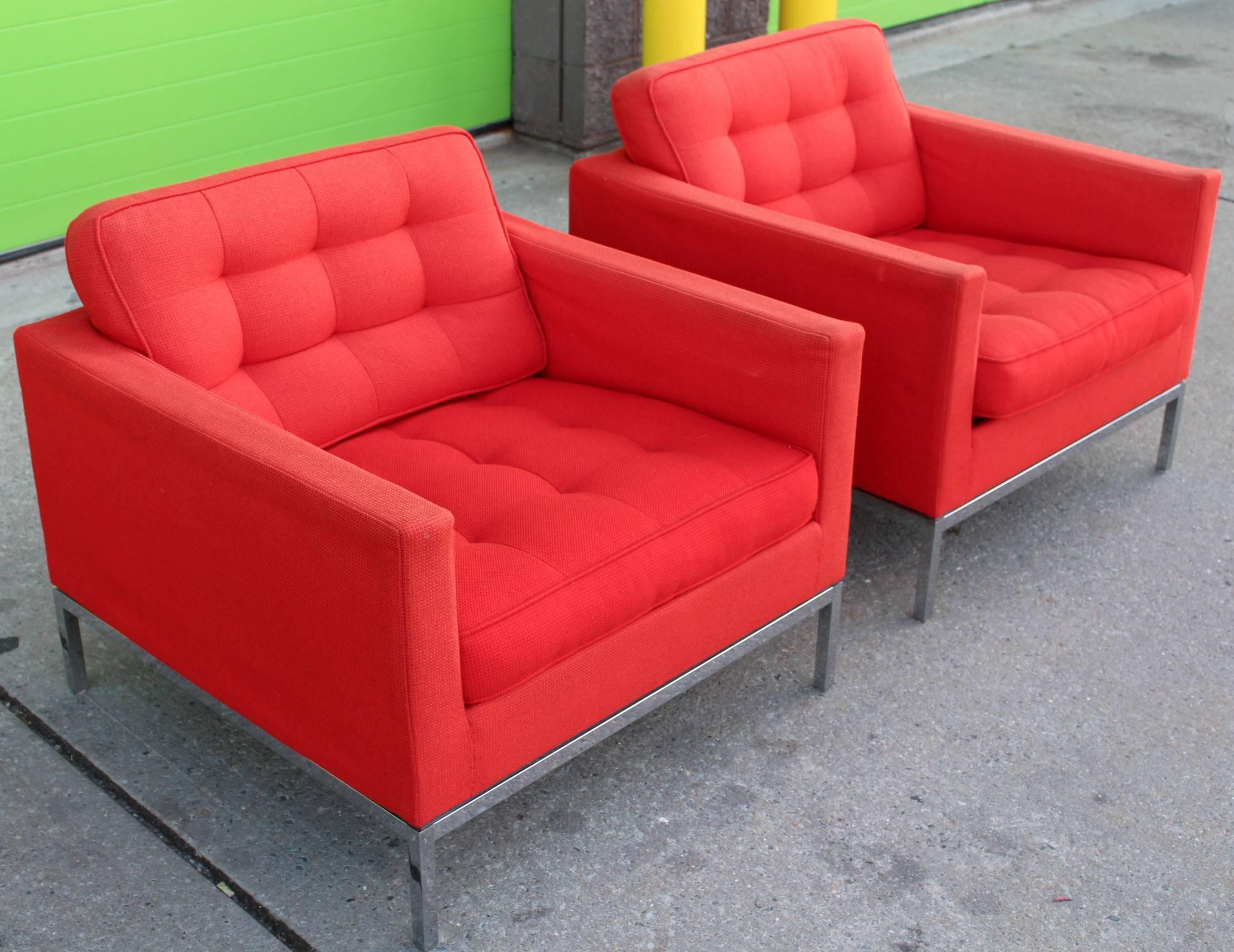 Two lounge chairs by Florence Knoll upholstered in red and made of chromed metal and wood. In good condition with no rips to upholstery but some signs of wear and staning. The cushions are removable. There is an original label and a sticker marked