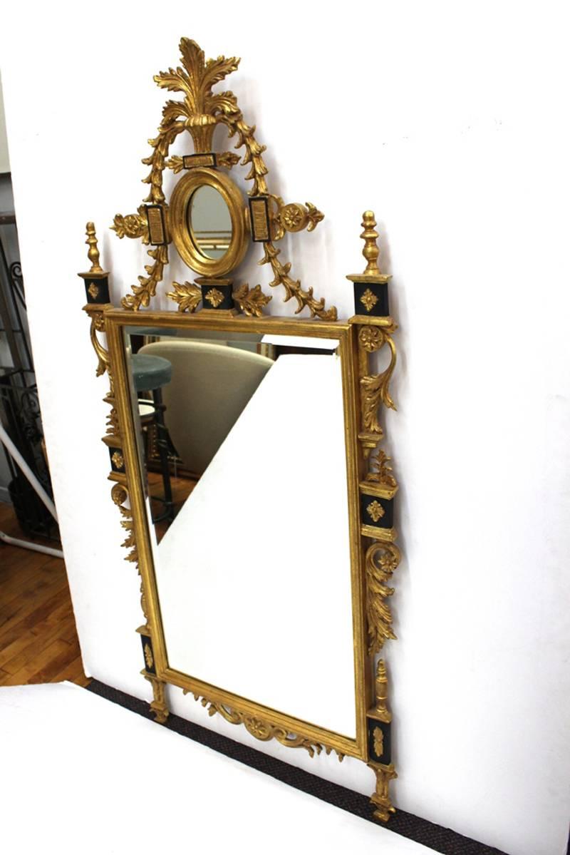 A gilt wall mirror in the Georgian style from the 20th century. Features florets, acanthus scrolls, and small oval mirror above the main wall mirror. In good condition consistent with age and use.