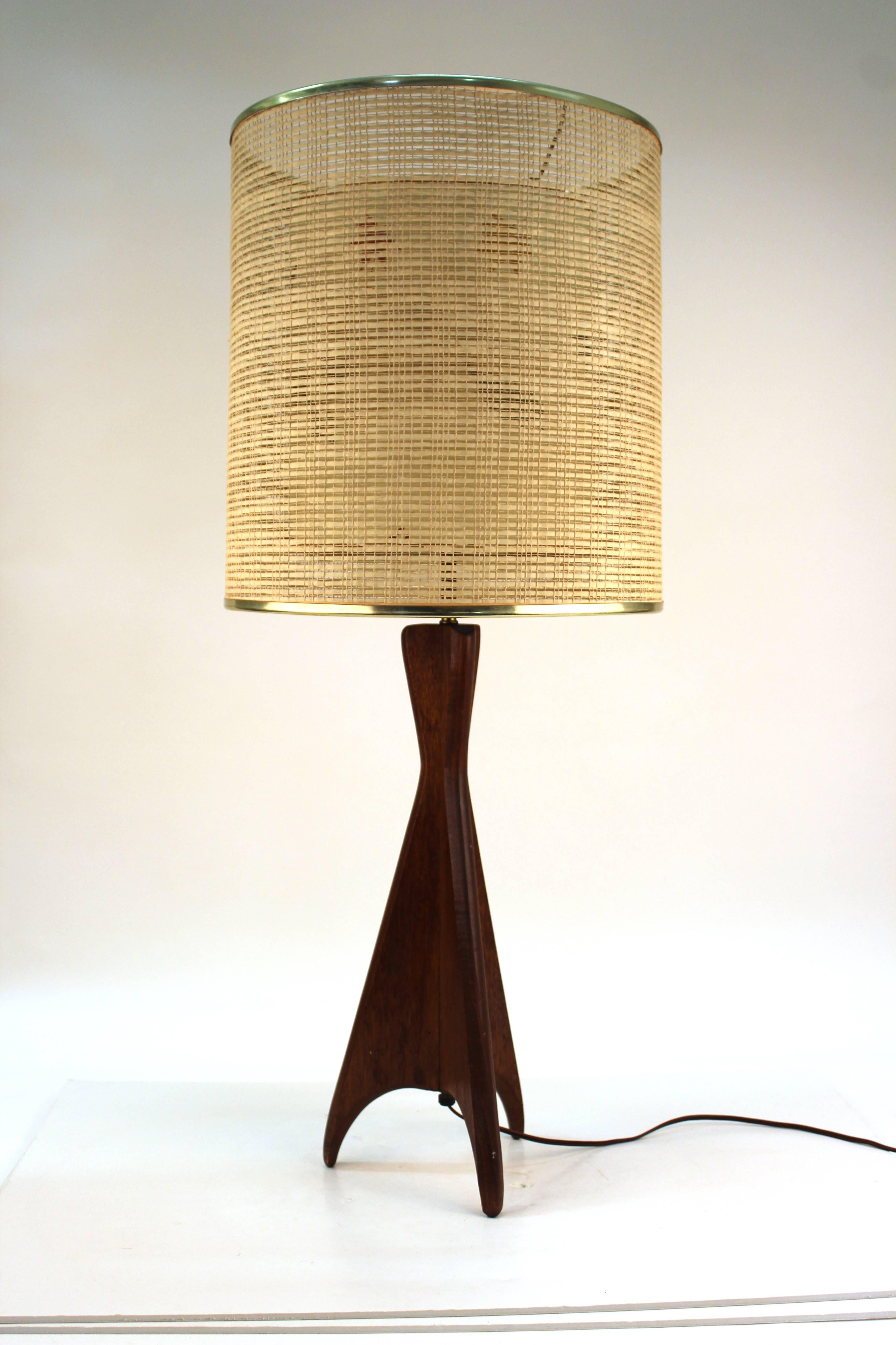 A Mid-Century Modern teak table lamp featuring a sculptural tripod base. The double shade's outer layer is made of raffia while the inner shade has pressed leaves. There is a large burn mark present on the inner shade. The rest of the lamp is in