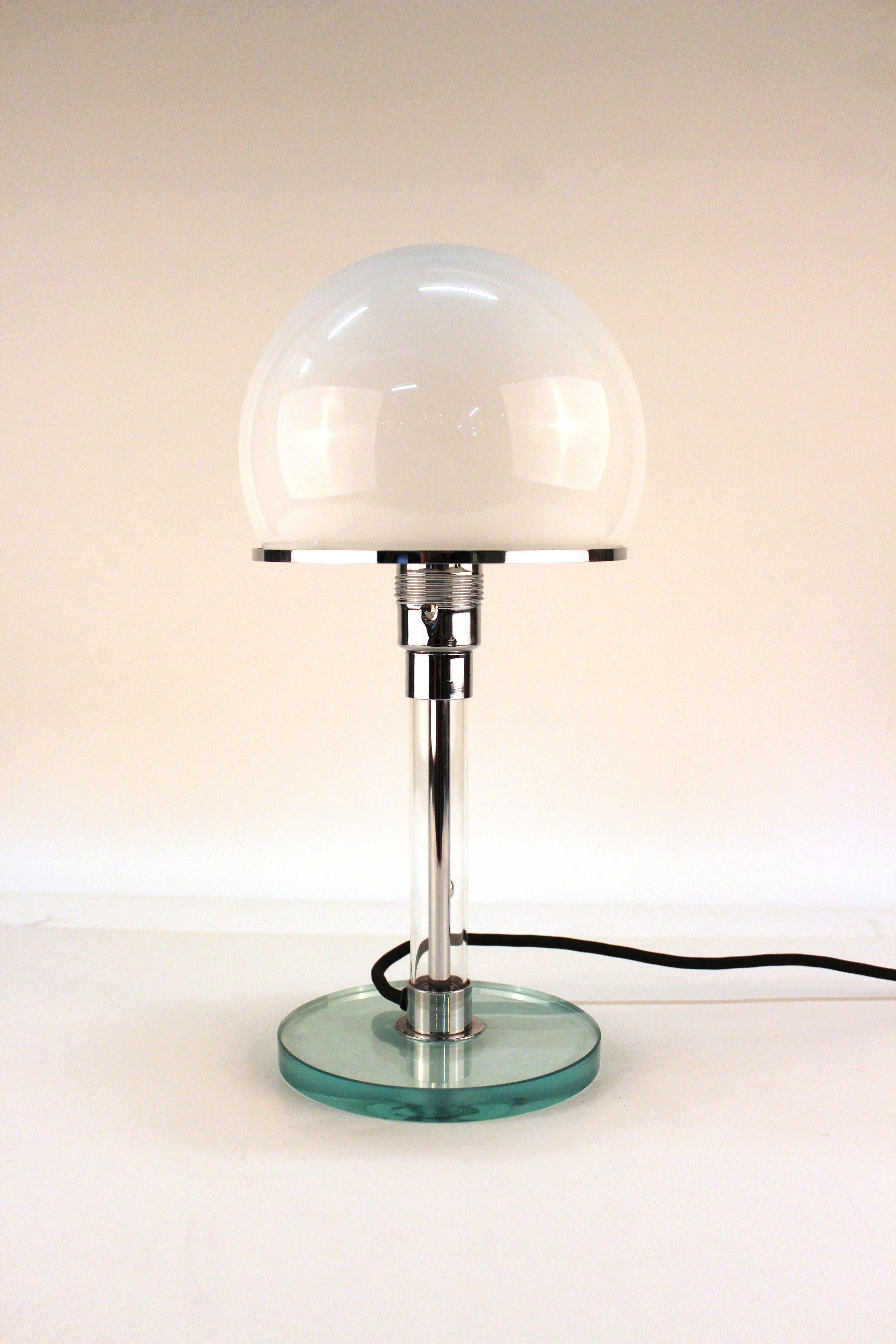 A Bauhaus table lamp designed by Wilhelm Wagenfeld and Karl Jucker on a blue Lucite base, chrome stem and domed glass shade in white. In very good condition.