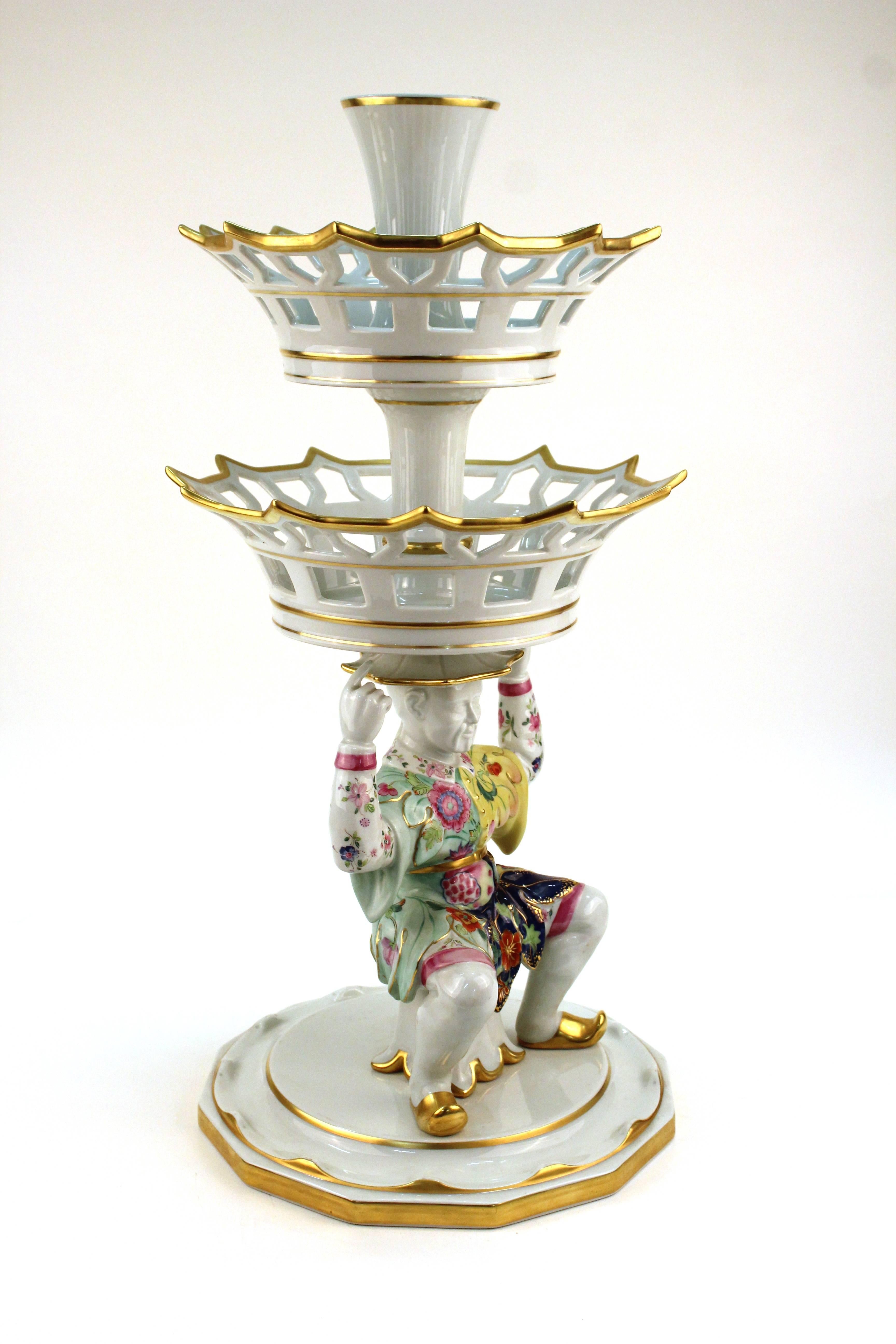 A multi-level epergne by Mottahedeh with a orientalist depiction of a Chinese man dressed in multicolored robes with the tobacco leaf motif. Include two gold trimmed baskets and several original labels. Hallmarks on the bottom of the base.