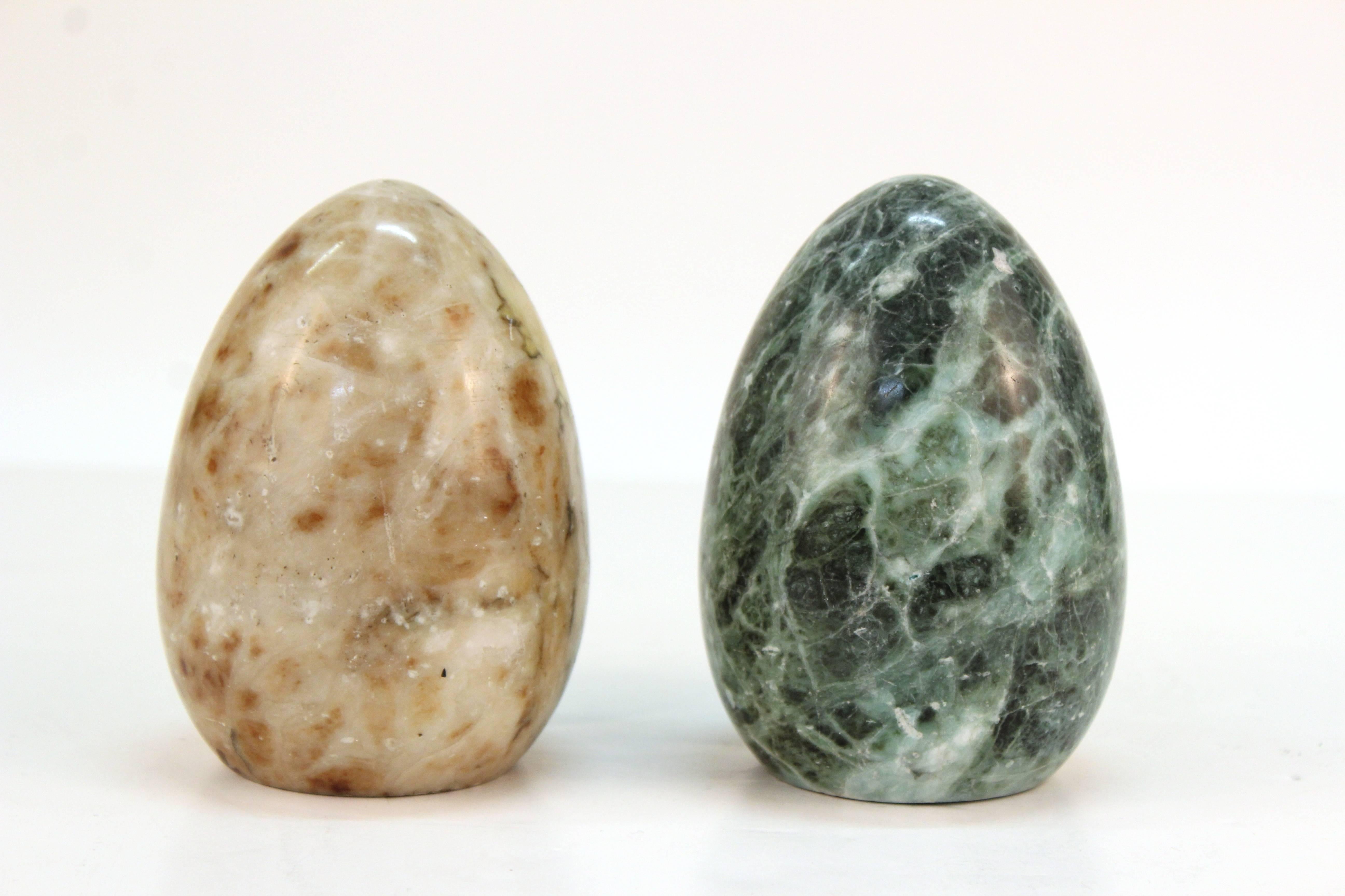 A pair of egg paperweights in marbled stone. One in cream with rust accents and another in mossy green; both are highly polished. Despite some wear due to material and use both items are in good condition.