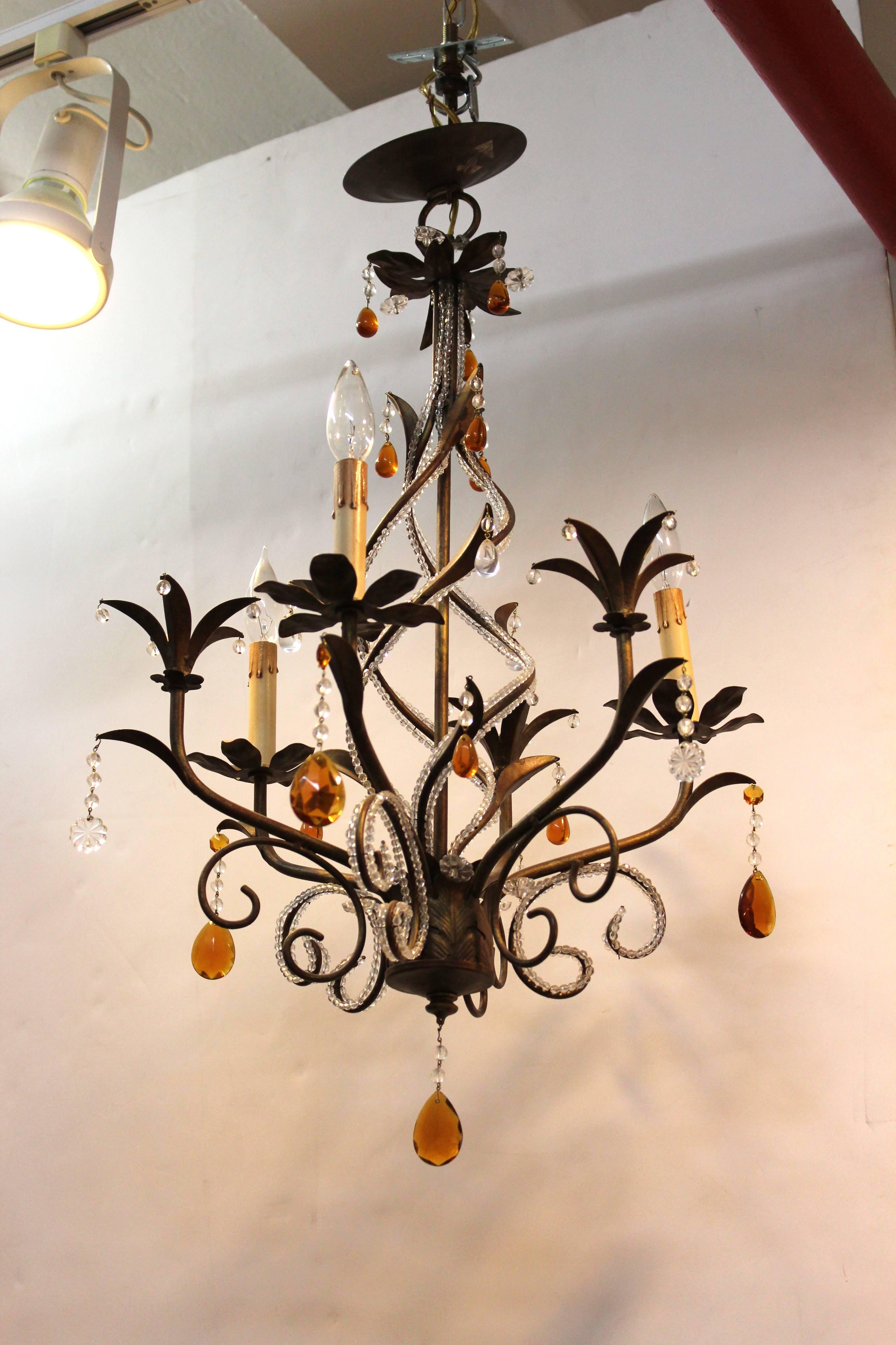 A chandelier made of patinated brass accented with clear crystal beads and faceted orange drops. Includes a unique helix centre shaft, faux candles and floral features. In good condition.