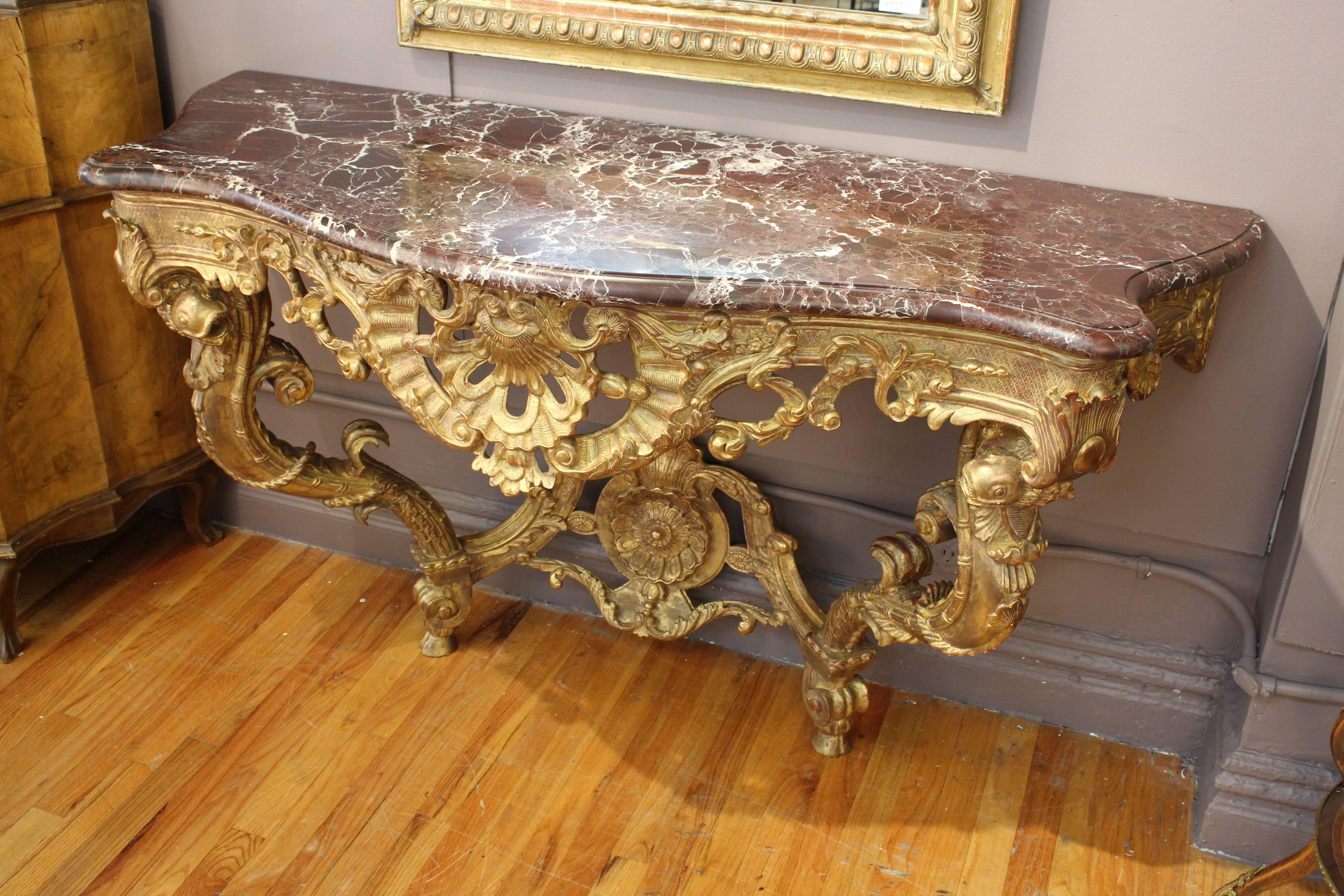 Pair of French giltwood consoles from the late 19th century-early 20th century in the style of Louis XV. Includes custom marble tops in deep red. Bottoms carved in detail with fish, acanthus leaves and large rosettes. Each curved leg stands on a