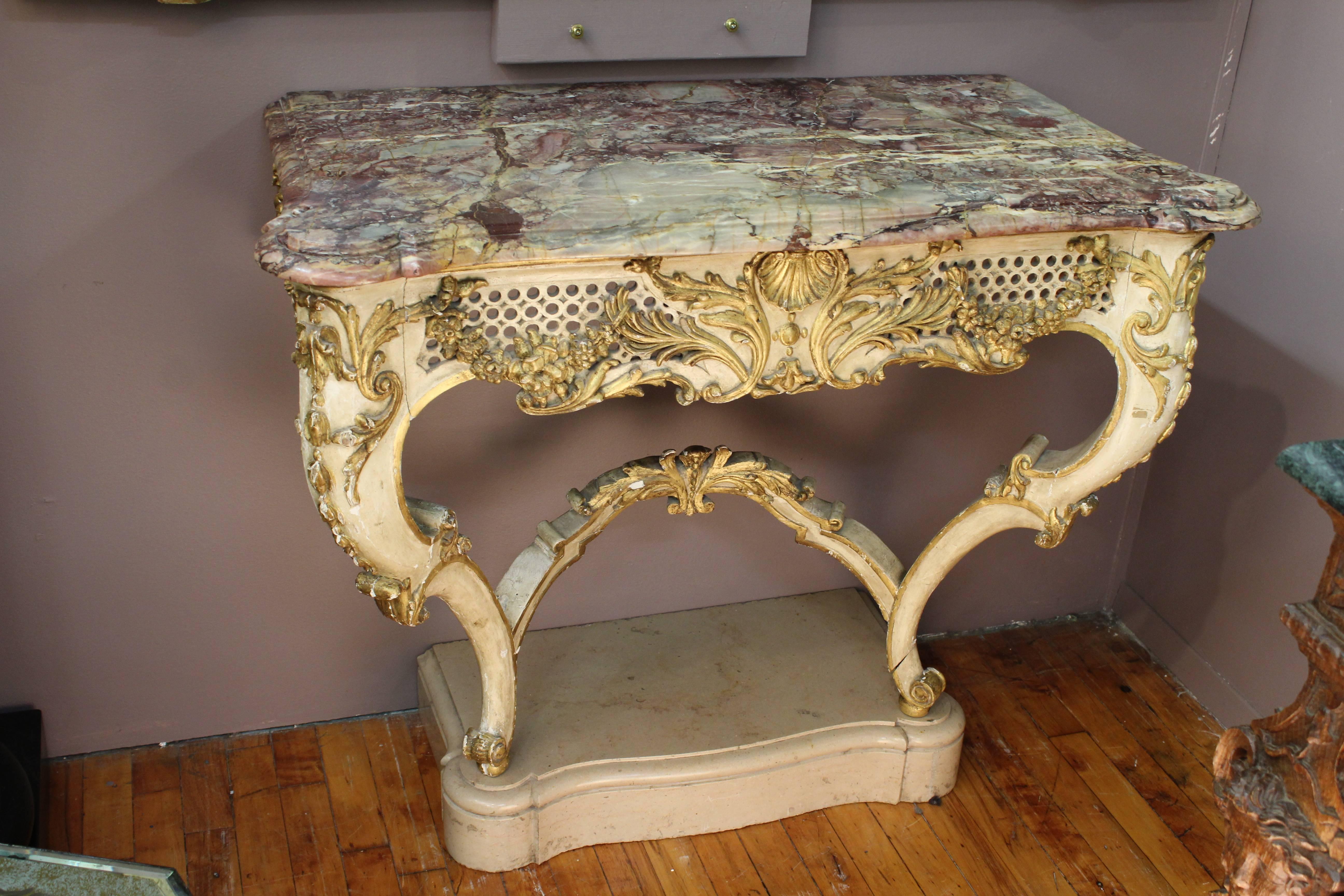 A French 19th century console table after the Rococo style with a purple marble top. The base is painted in white with gilt accents and stands on curved legs atop a marble piece. The console is carved with a circular motif, garlands, acanthus leaves