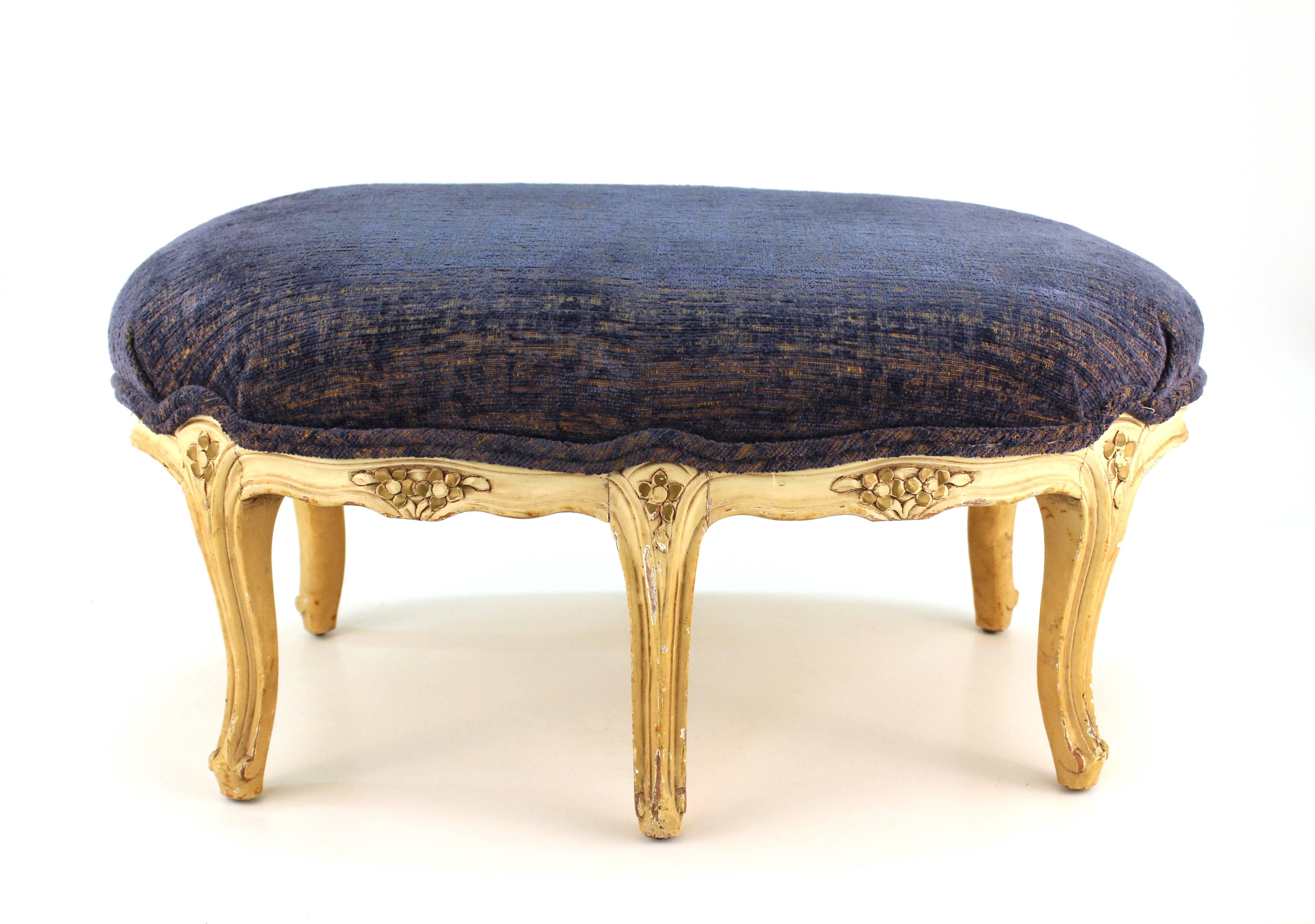 A long oval footrest on six legs. Crafted in pale wood with etched detail and floral motif. Covered in soft blue upholstery. The item is in good condition.