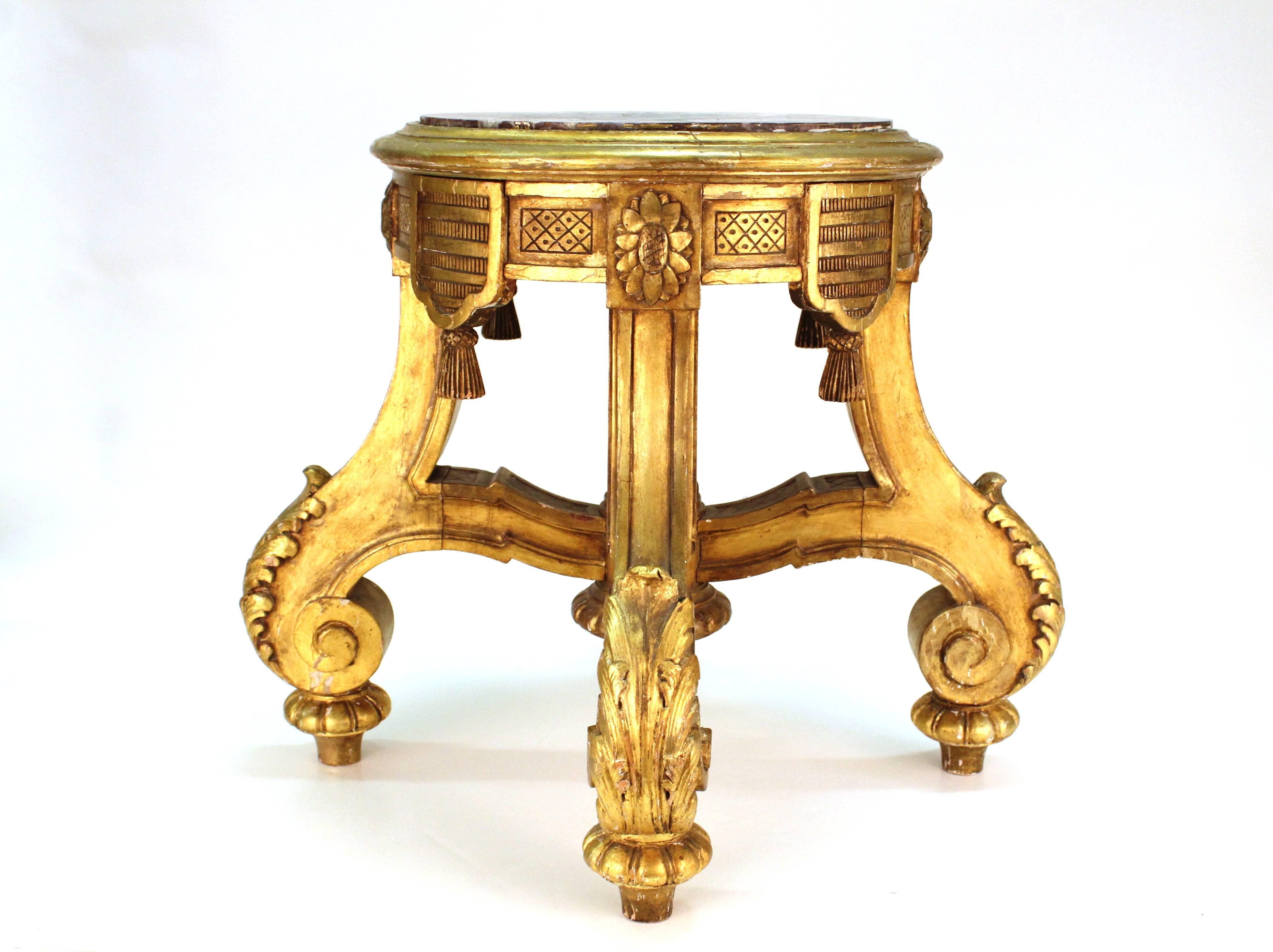 A pedestal or stool in giltwood with a marble top. Stands on four scrolled feet accented with acanthus leaves. The circular top is framed in rosettes and carved tassels. The item is in good condition with minor wear appropriate to age and use.