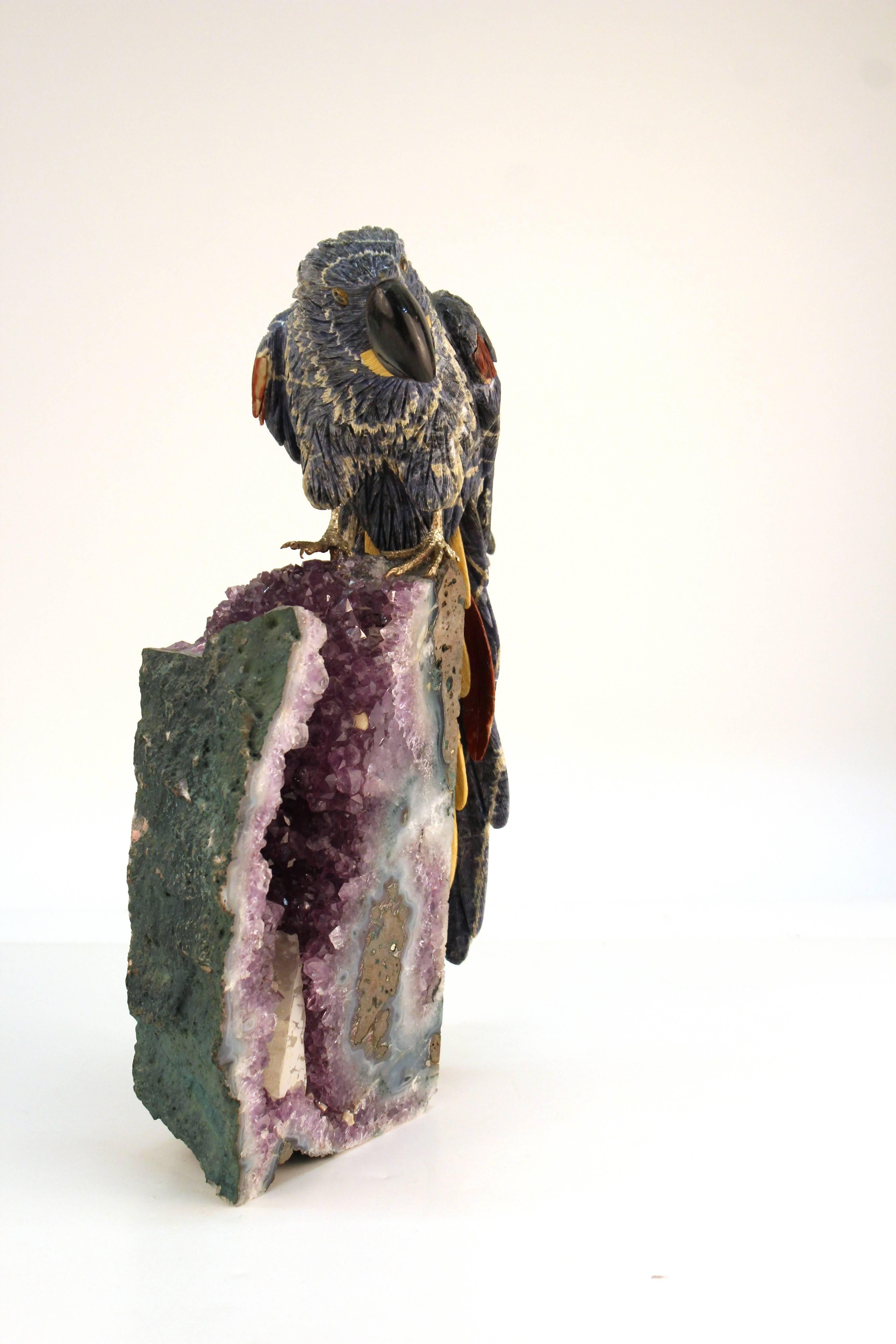 A sculpture with a large parrot crafted in different colored marbles and stones. The bird is mounted on a large piece of sliced amethyst crystal. Some small cracks and missing bits on the tip of the bird's feathers. In good condition appropriate to