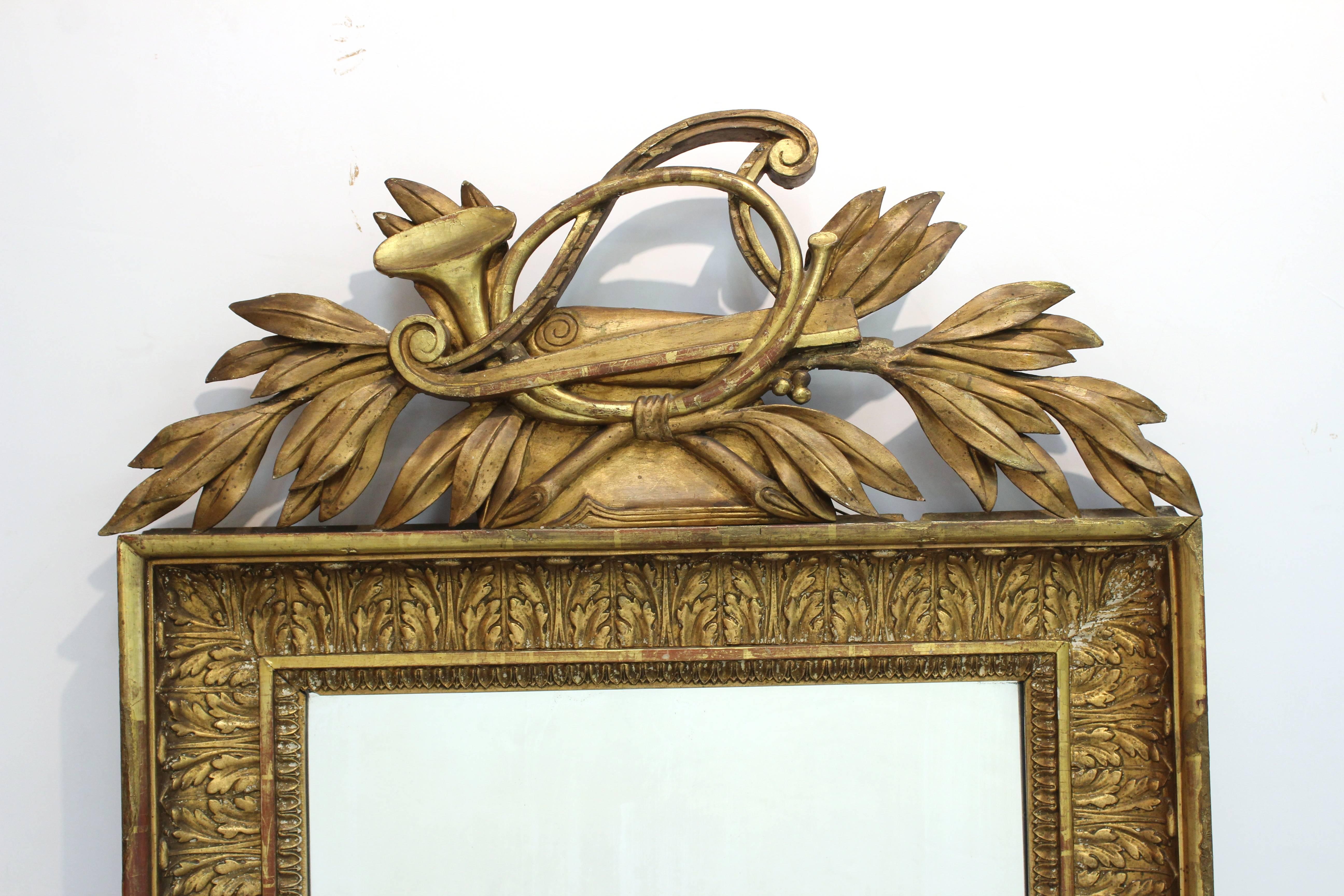 A giltwood neoclassical wall mirror framed in an acanthus leaf pattern. The mirror is topped with laurel leaves, a horn and stringless harp. Some wear to the gilt and wood but in good condition.