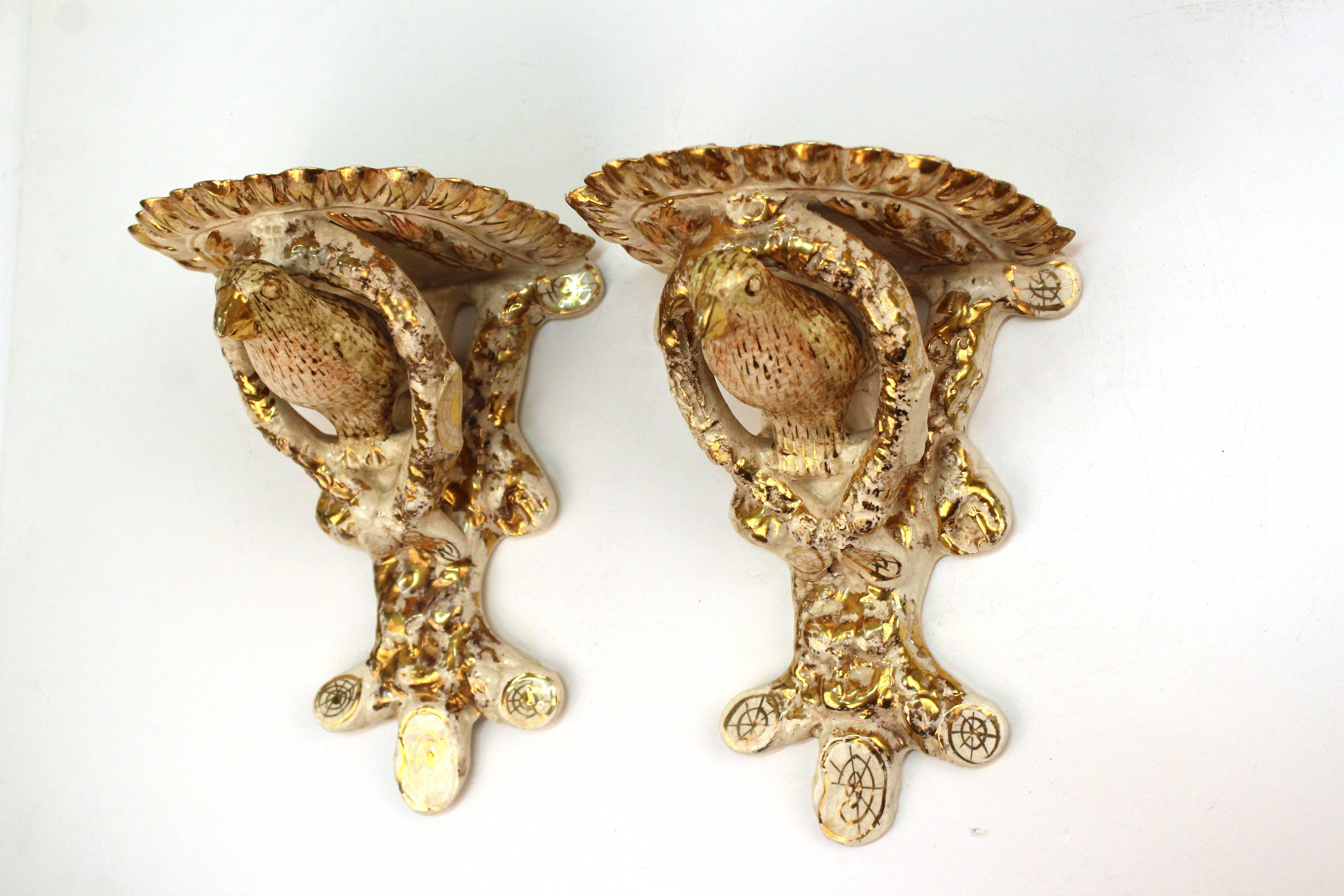 A pair of ceramic sconces with gold accents on white. Painted to look like birds sitting among tree branches. The birds feature gold beaks with pink washed bellies and pale green feathers also highlighted in gold. Minor wear to the ceramic due to