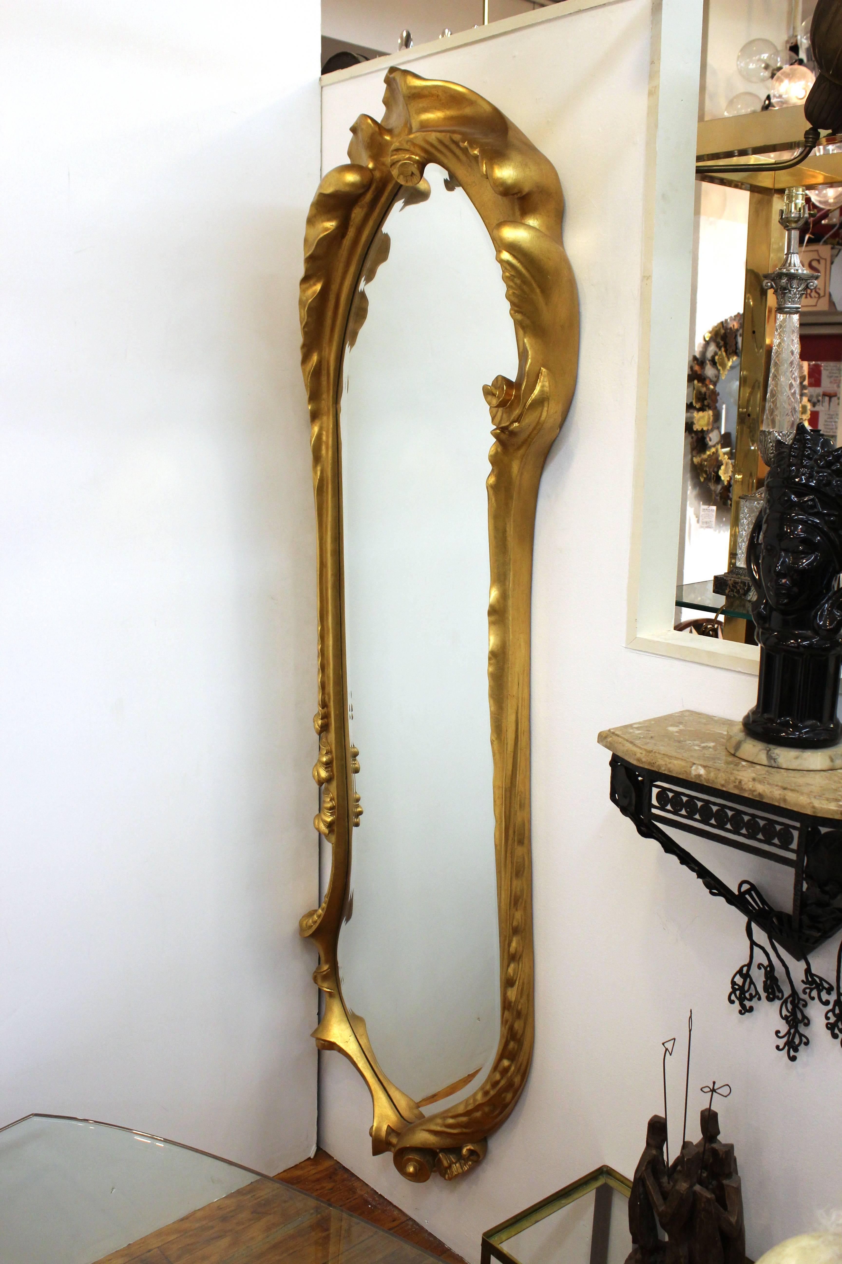 A monumental full-length wall mirror with an opulent carved giltwood frame, made in the 20th century. The frame presents an ornately carved naturalistic design with swirls and organic foliage. Good vintage condition consistent with age and use.