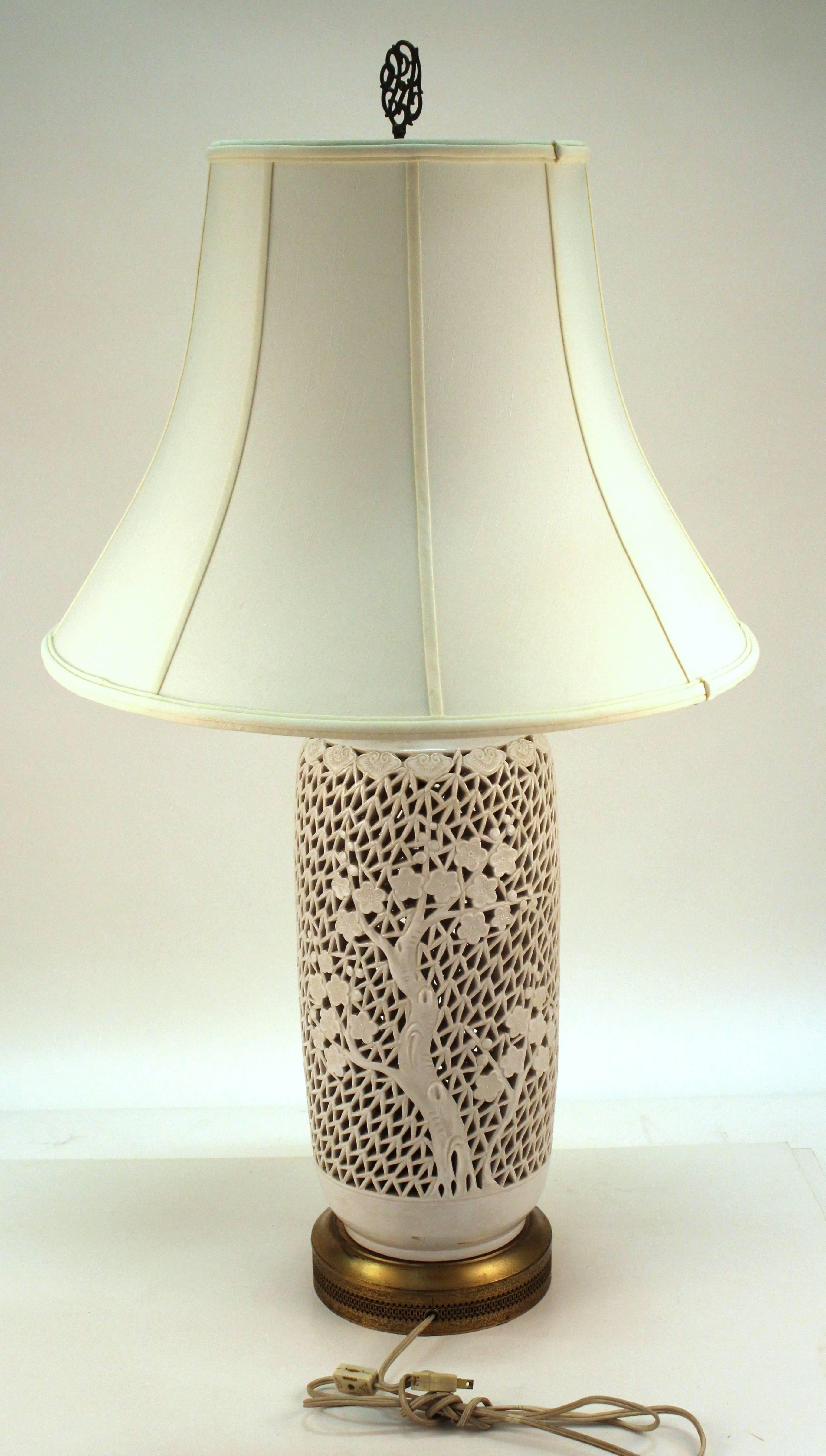 1920s blanc de chine ceramic table lamp in perforated blossom pattern. The brass base also features cutout detailing as well as a decorative etched pattern. In very good condition. 111229.
