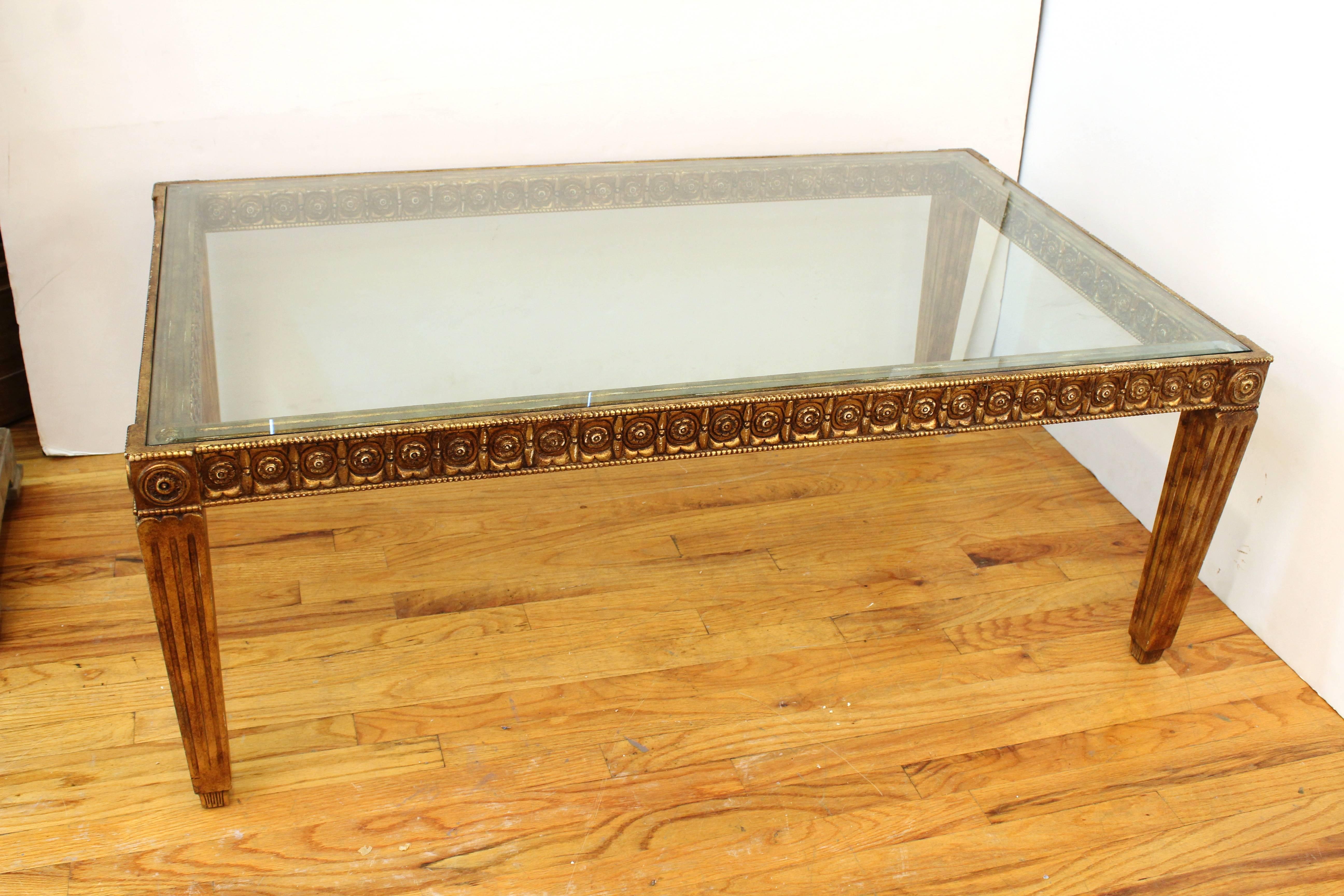 A giltwood coffee table with glass top dating from the 20th century but in a 19th century style. The table's frame is carved with beads and a rosette pattern on both the interior and exterior. The rectangular table stands on four column like legs.
