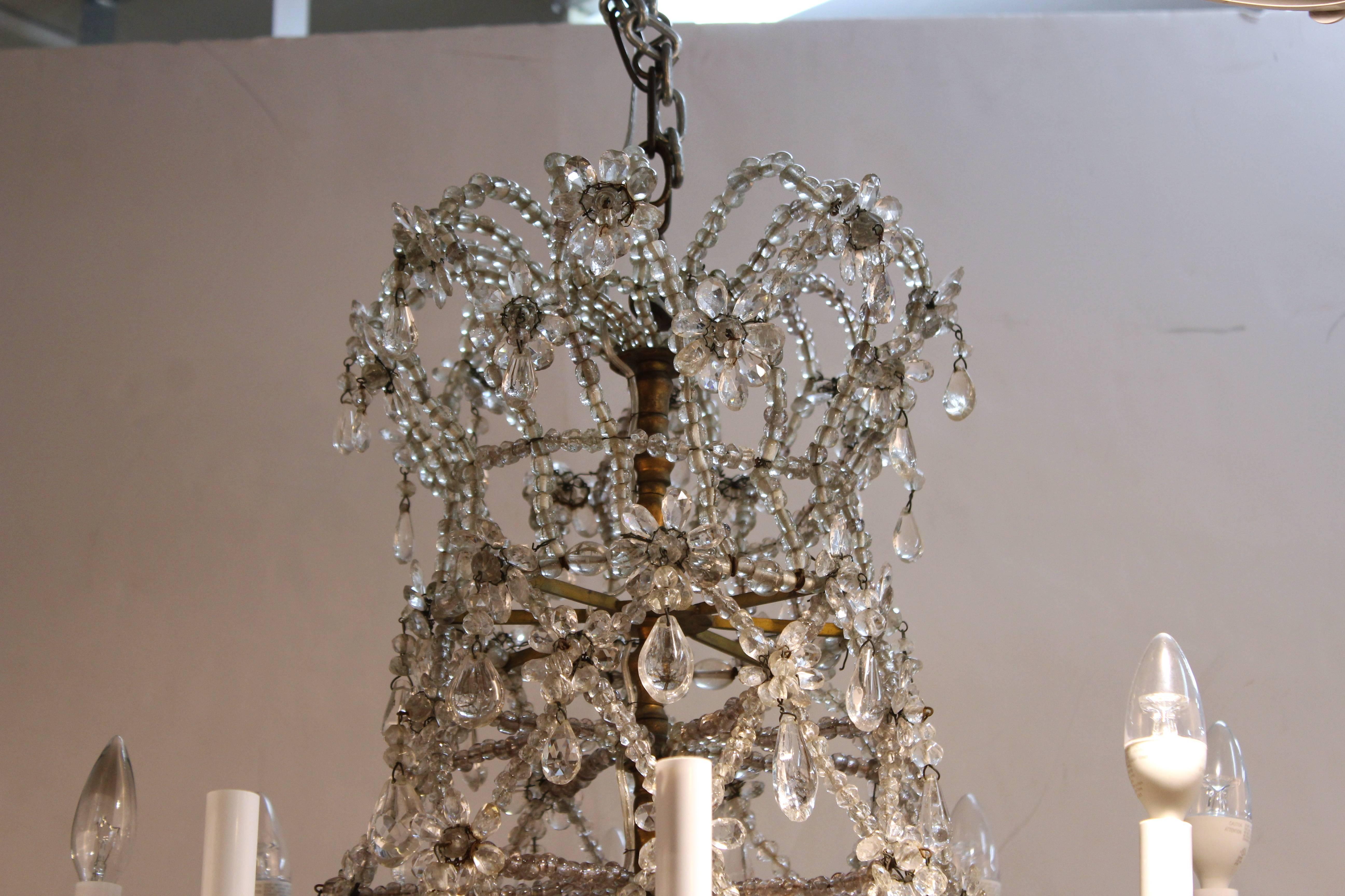 A rock crystal chandler dating between the 18th and 19th century crafted in Austria. The chandelier features eight arms with faux candle sockets. The patinated brass frame is adorned in a net of crystal beads with rosettes and clear drops. The