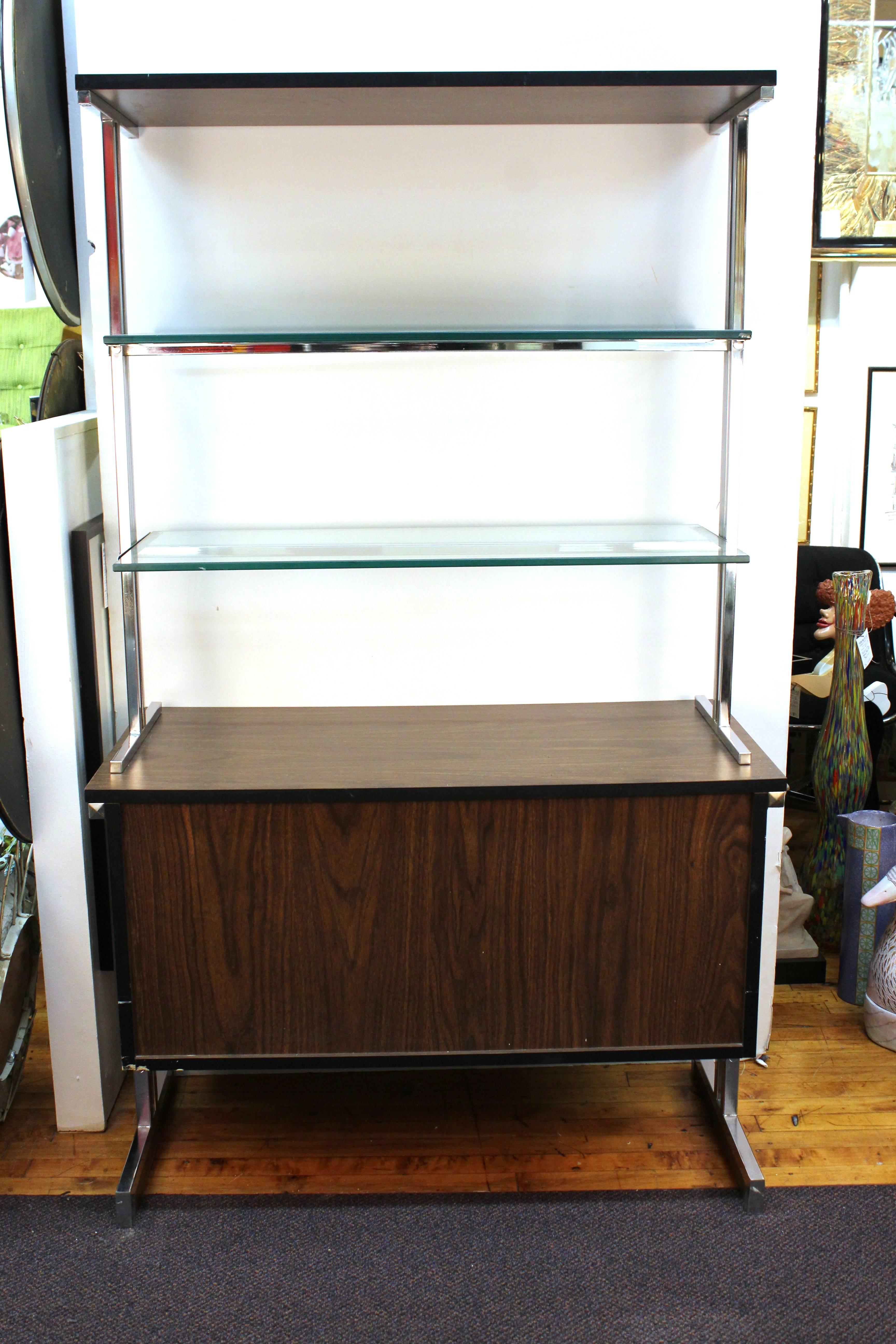 Pair of matching etageres or cabinets produced during the 1960s after Milo Baughman. Manufactured with a dark stained wood base mounted on chrome legs. Both include a detachable section with glass shelves on chrome. Despite some minor scratches to