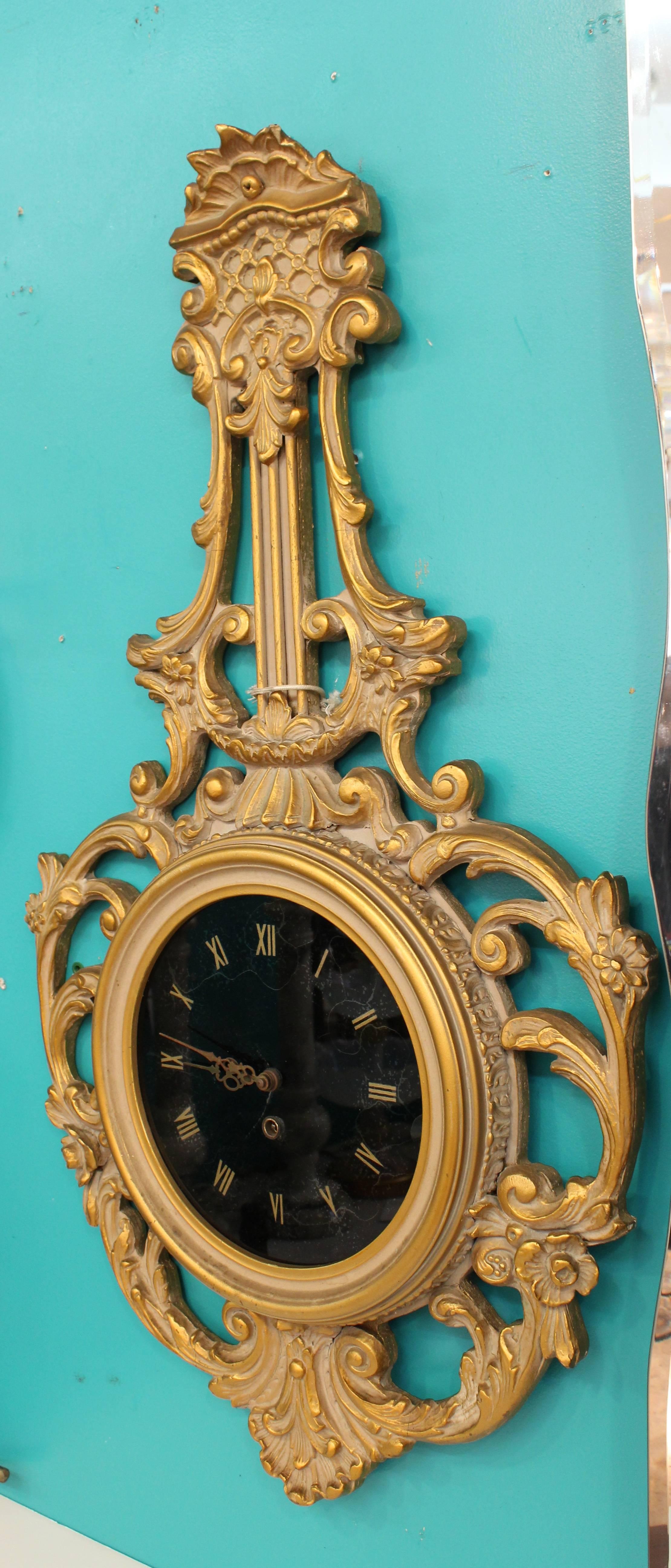 A decorative black glass clock with églomisé roman numerals. The piece is held in an elaborately carved drop frame. The clock winds up with key. In good condition. 