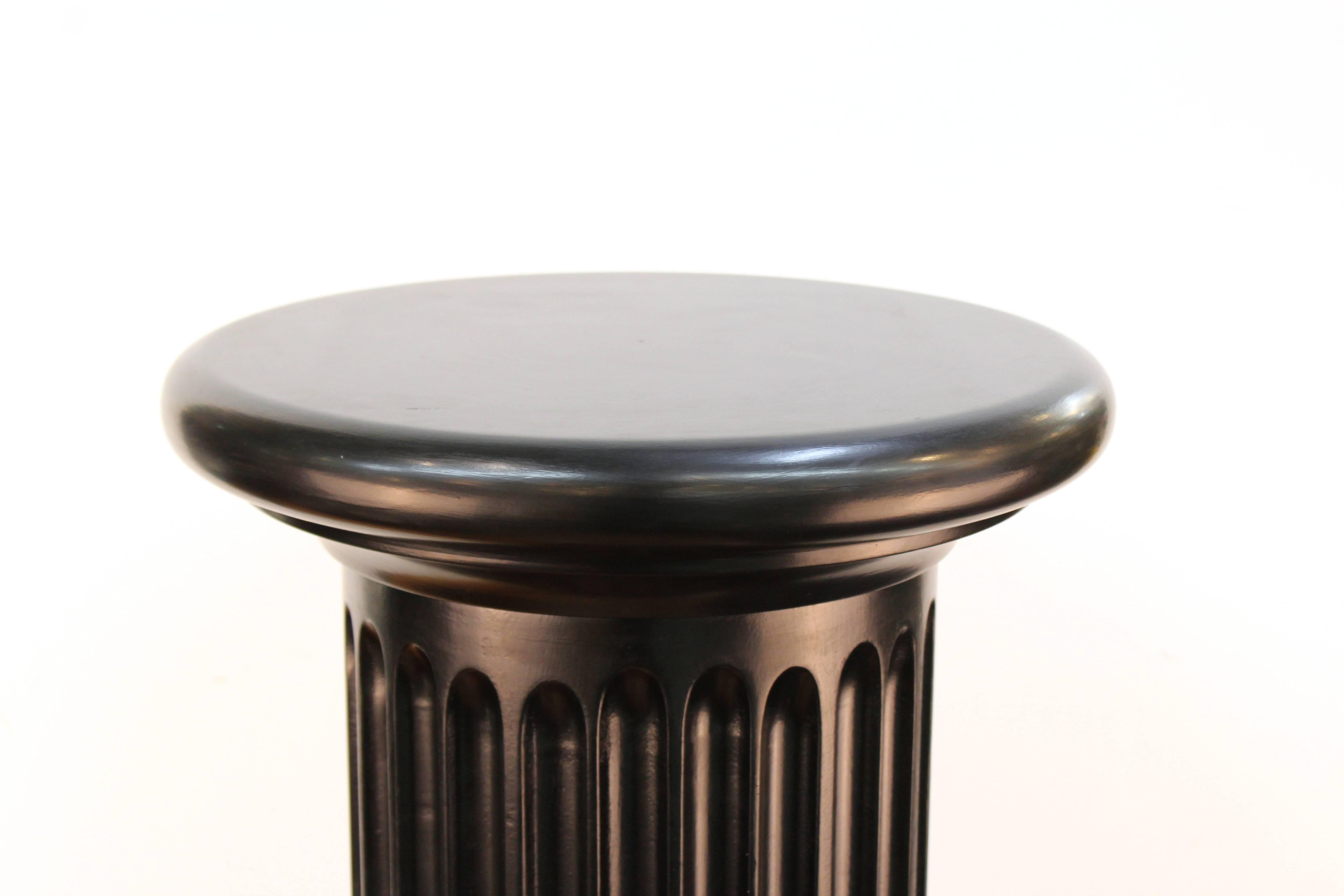 Two tall fluted columns in ebonized wood. Each Doric-style column has a base, fluted shaft, and capital all in ebonized wood with a smooth finish. The pair remains in excellent condition, consistent with age and use. The included measurements are