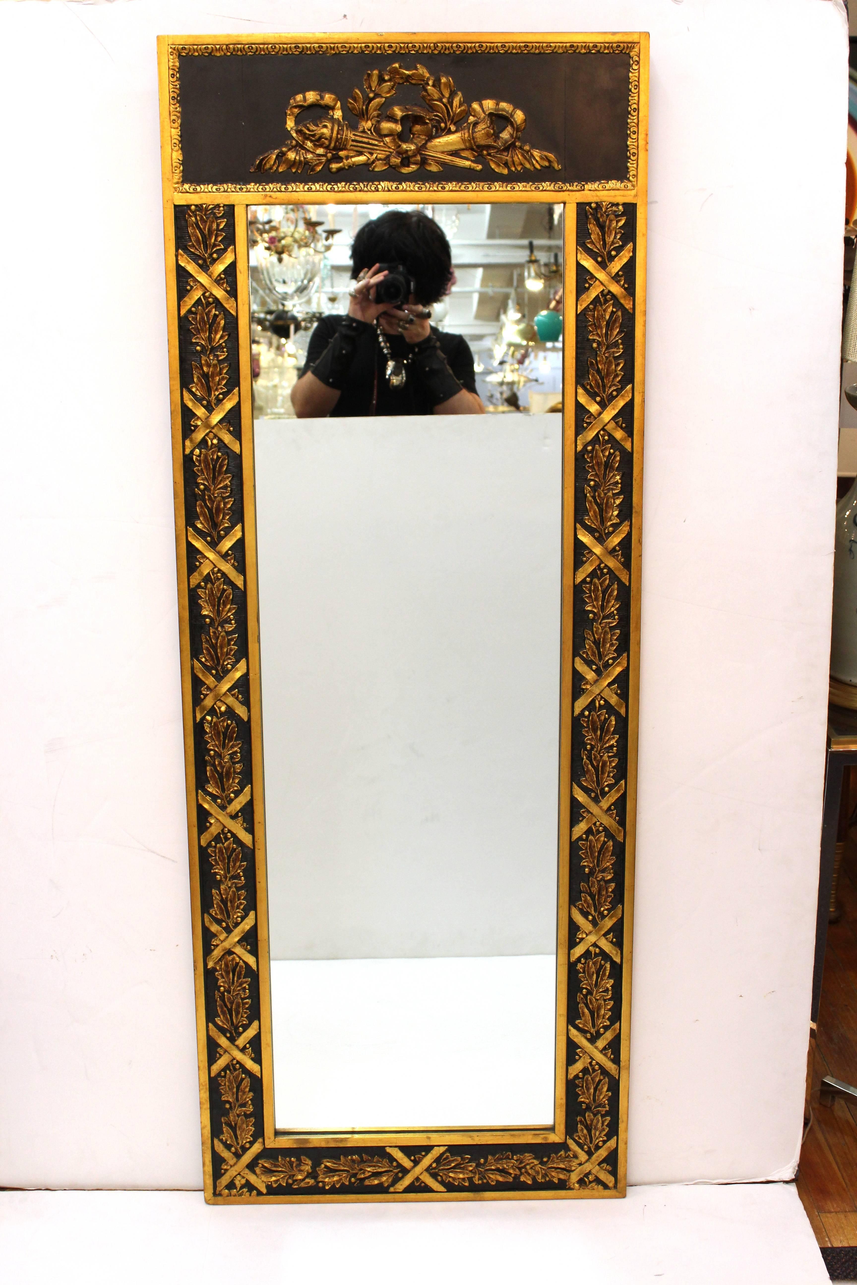 Long rectangular neoclassical mirror in black and gold. Hand-carved in France during the 1940s with neoclassical motifs such as the laurel leaf border. The top is decorated with laurels and trophies. The mirror is in very good condition.