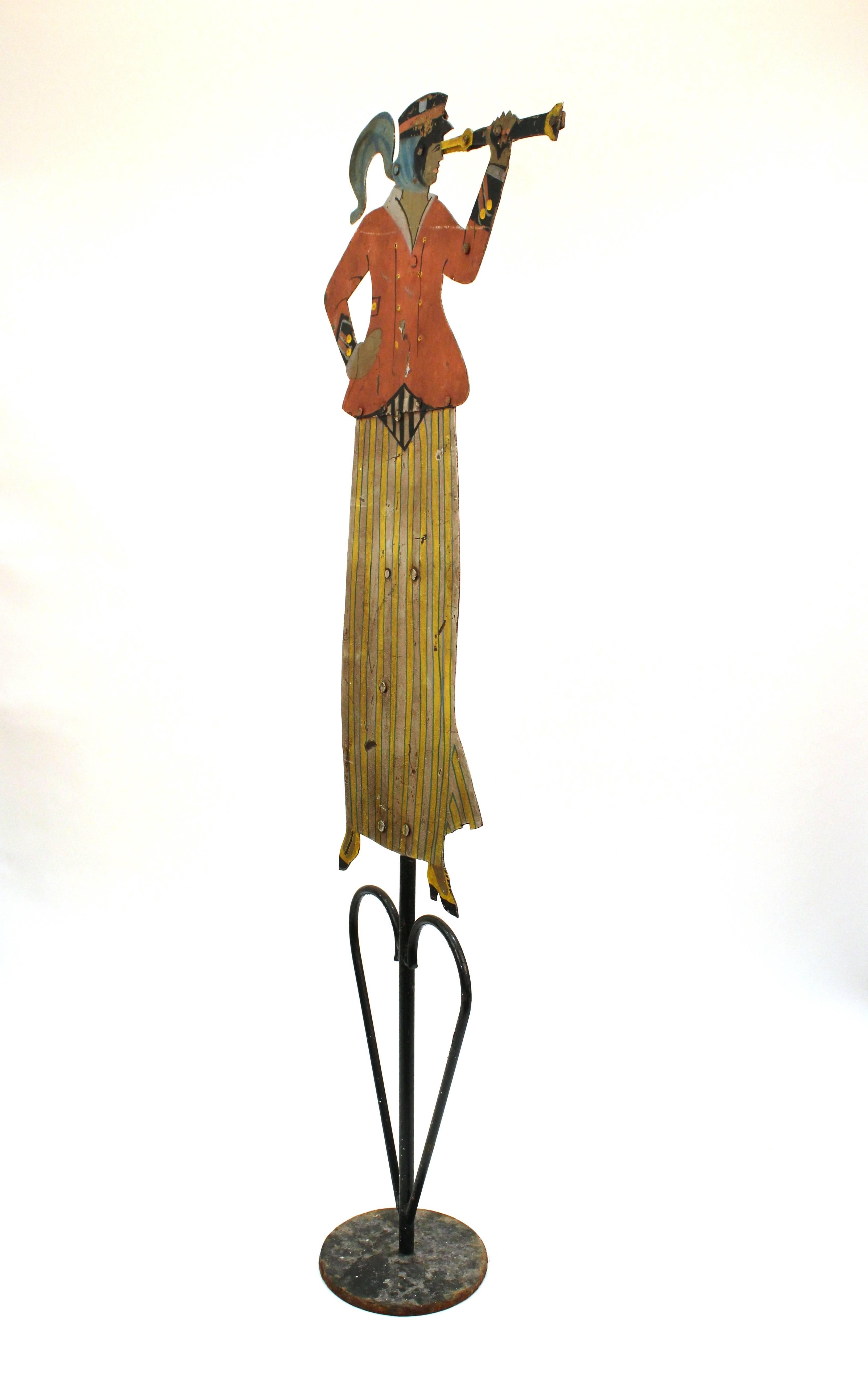 Antique iron weathervane depicting a woman looking through a spyglass. The woman is dressed in early 20th century attire including a yellow striped skirt and red jacket. Includes a wrought iron stand. Age appropriate surface wear but in good