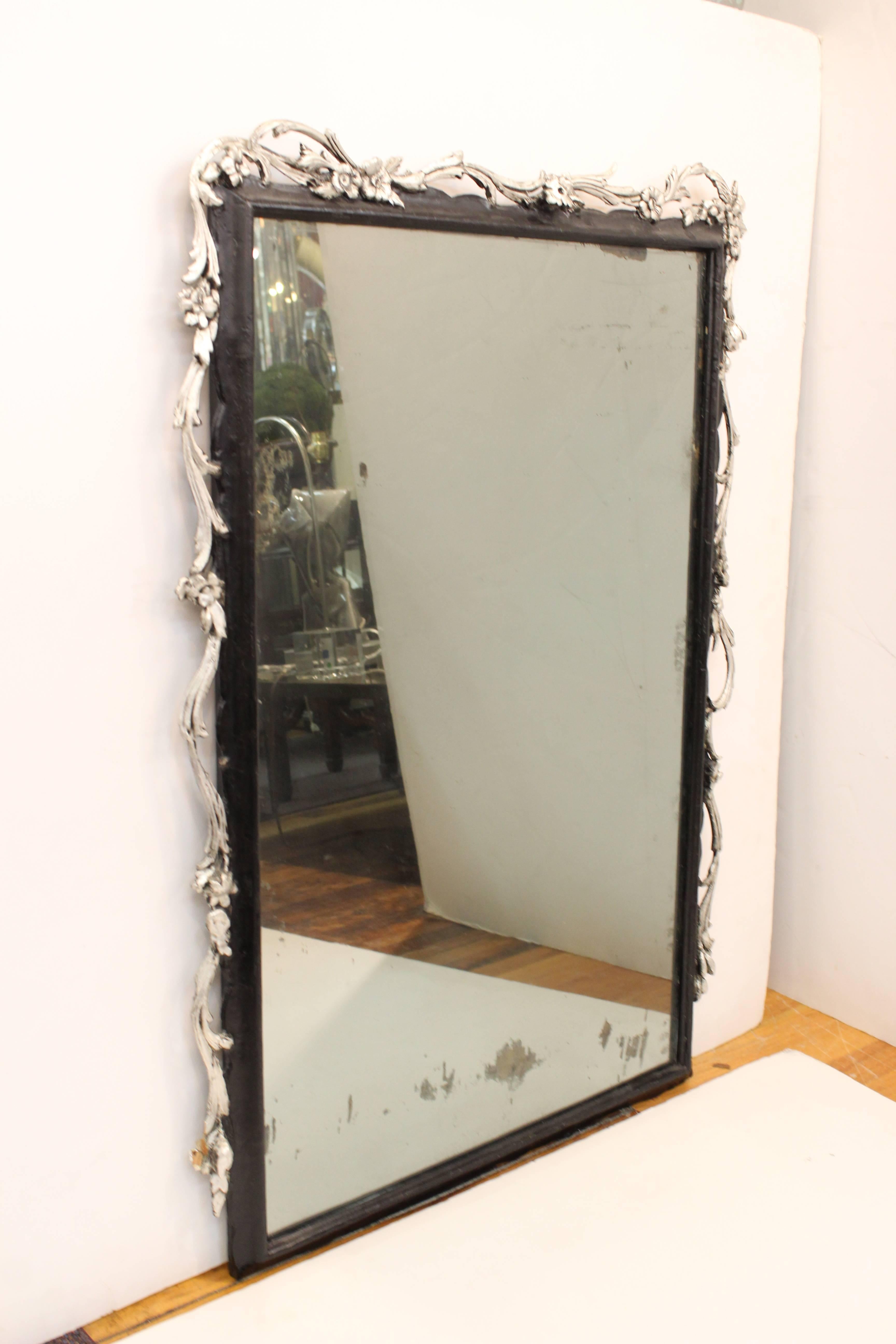 A rectangular wall mirror in a black painted frame. The crown and sides of the frame are accented with silver-tone painted vines and flowers. Some visible spotting to the mirror and minor wear to the frame. The piece is in good condition.
