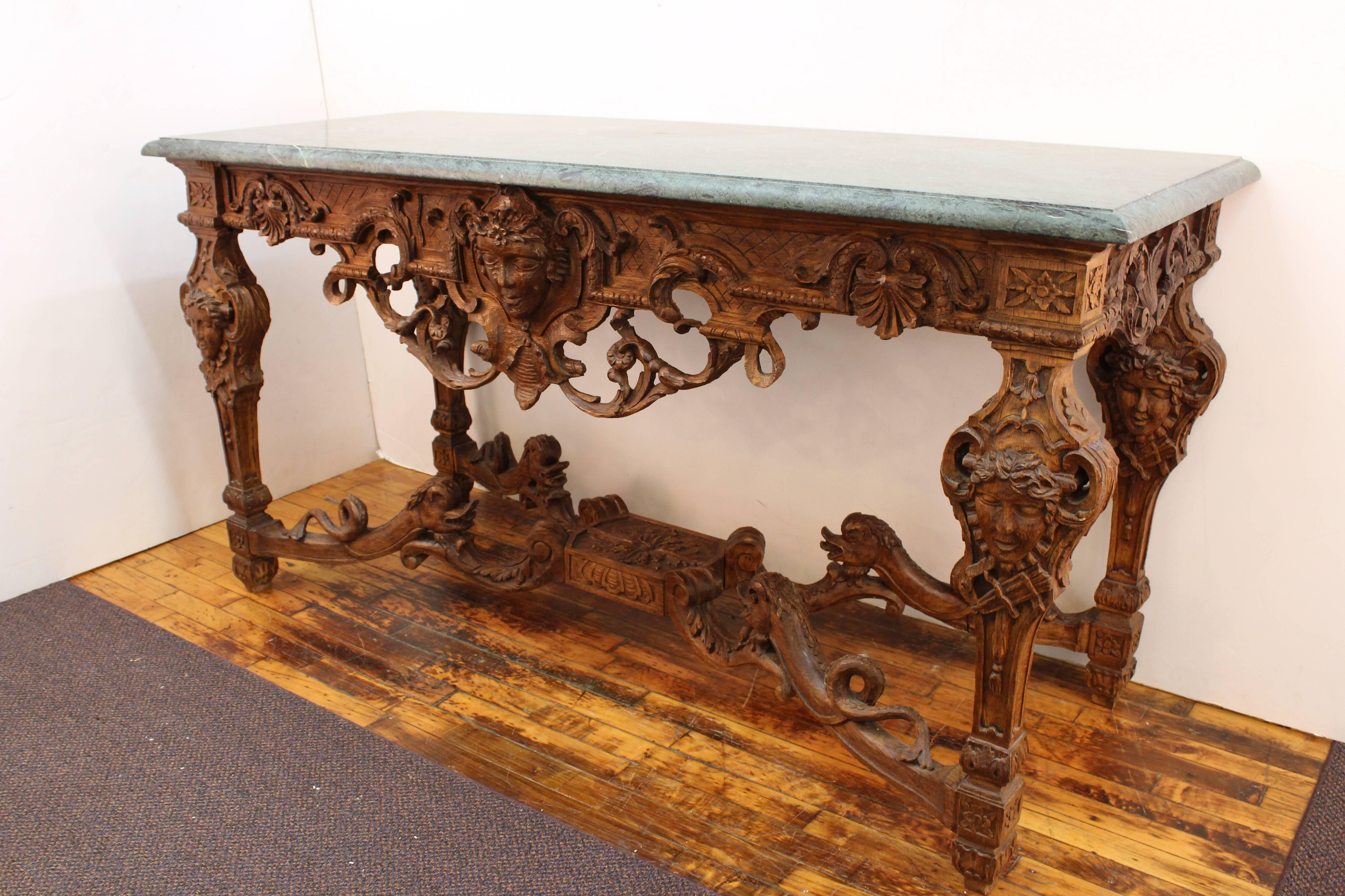 An antique Louis XIV style console table in untreated wood. Sculpted with faces, scroll work, architectural elements, dolphins, acanthus leaves and other flora. The table top is made of green marble. Wear consistent with age and use. In good