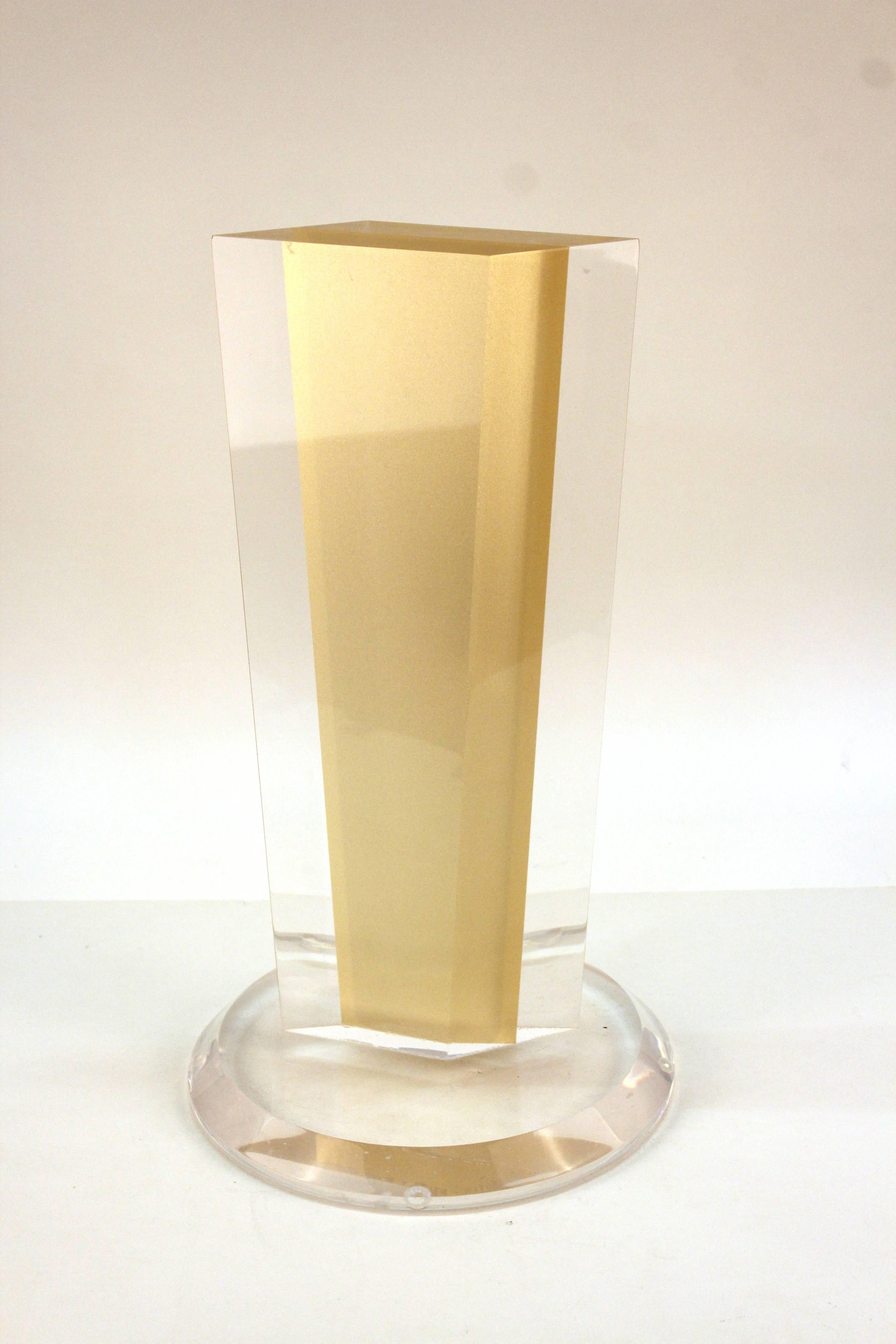 A long Lucite sculpture on circular base. Features a tall cream block encased in clear Lucite shaped in a off-kilter rectangle. Wear consistent with use and material. The piece is in good condition.