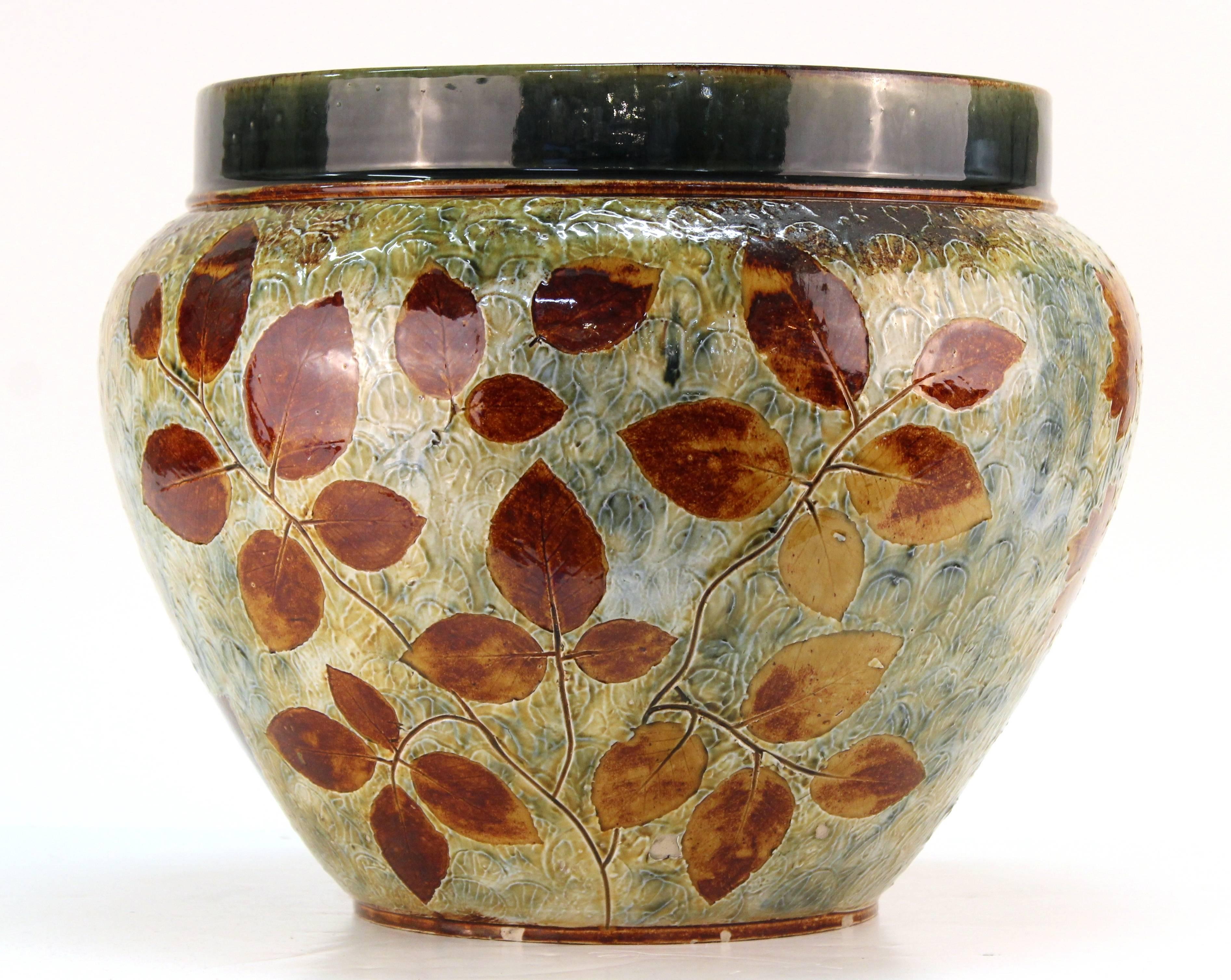 Large sized Doulton planter in a light green with reddish orange leaf motif. Three different types of leaves are featured, each on 1/3 of the exterior. There is also a dark green band around the top of the planter. Marked 