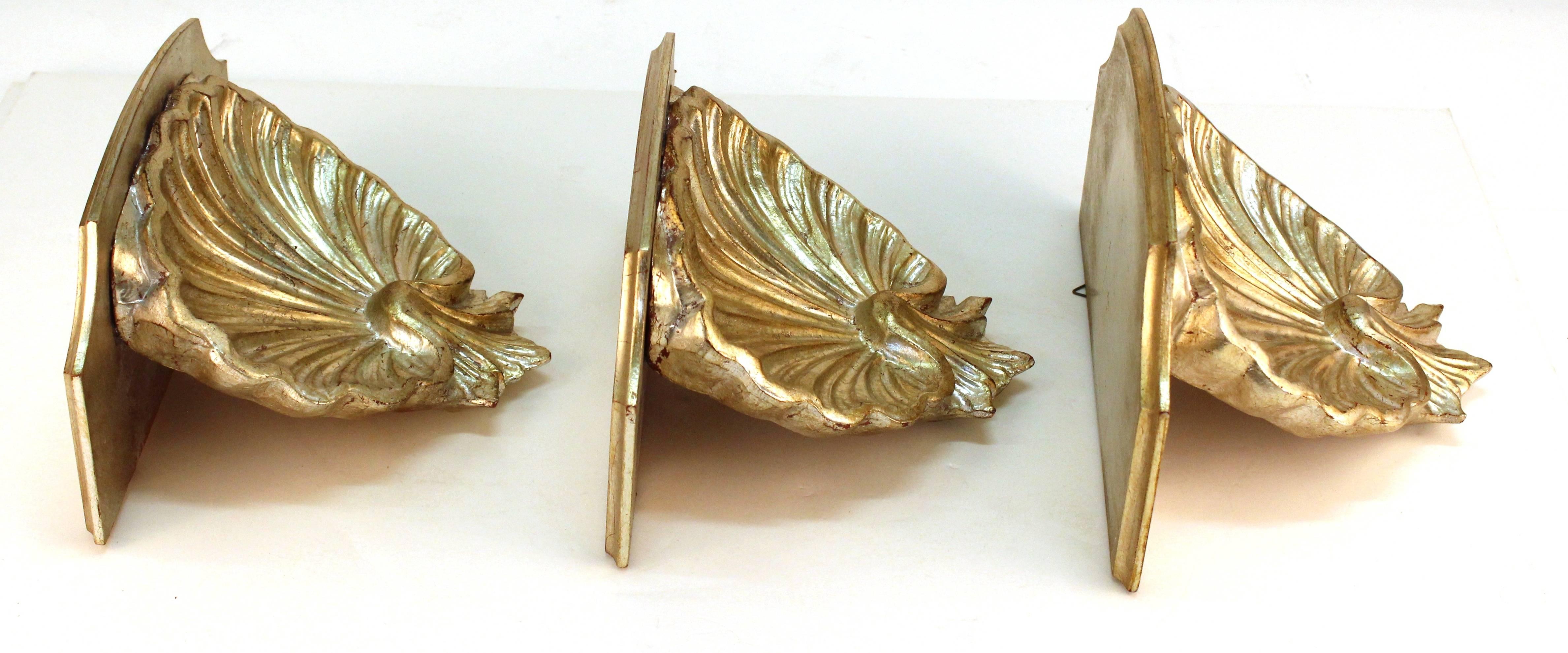 Shelf wall sconces with shell shapes in wood, painted silver. Each of these three wall sconces features a flat shelf on the top and scalloped shell form underneath. Each of these shelves is in good vintage condition and has wear consistent with age