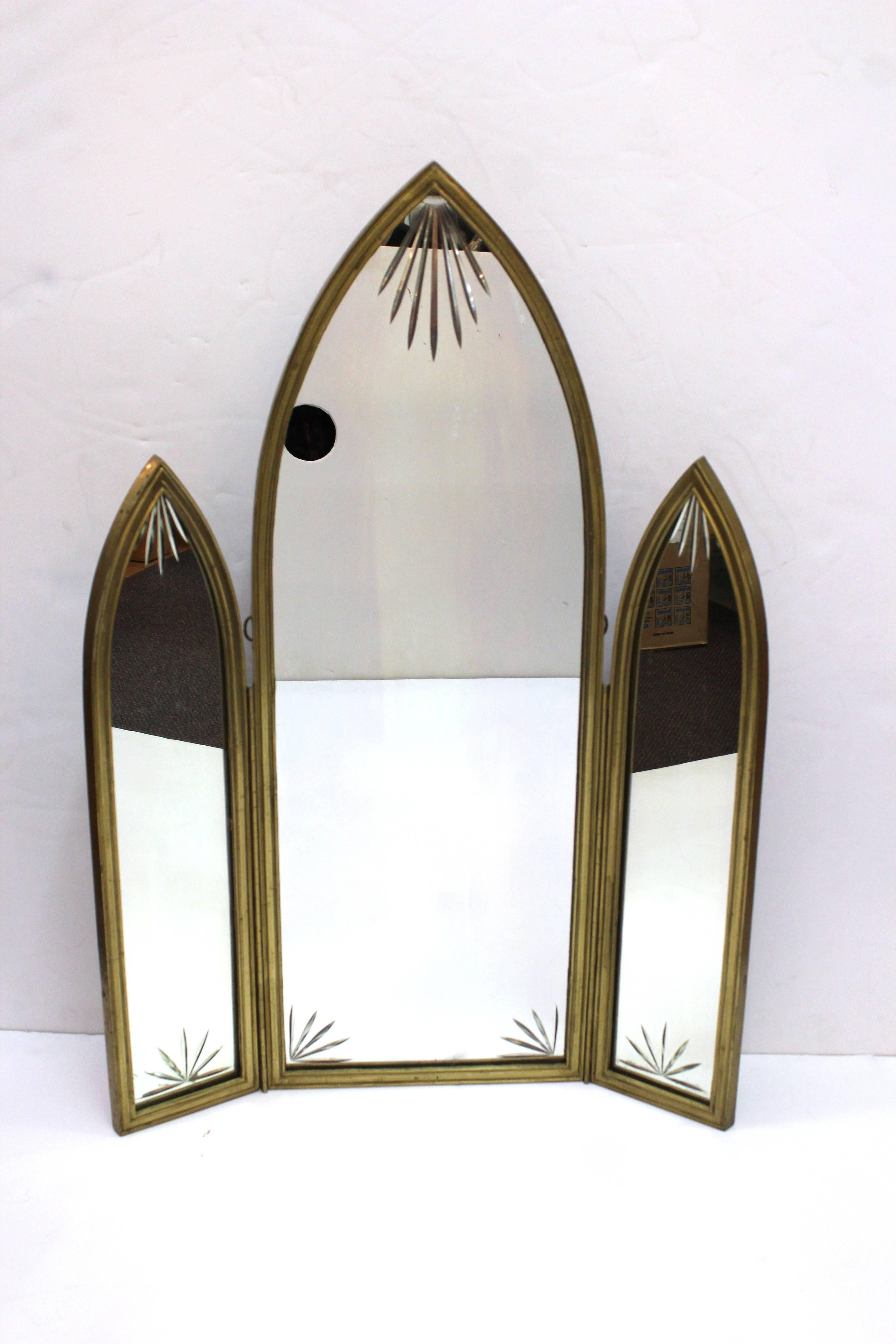 A French Art Deco triptych mirror in bronze with one central panel flanked by two smaller panels that fold outwards on a hinge. Each corner of the glass features a sunburst motif. The mirror is in good vintage condition and has wear consistent with