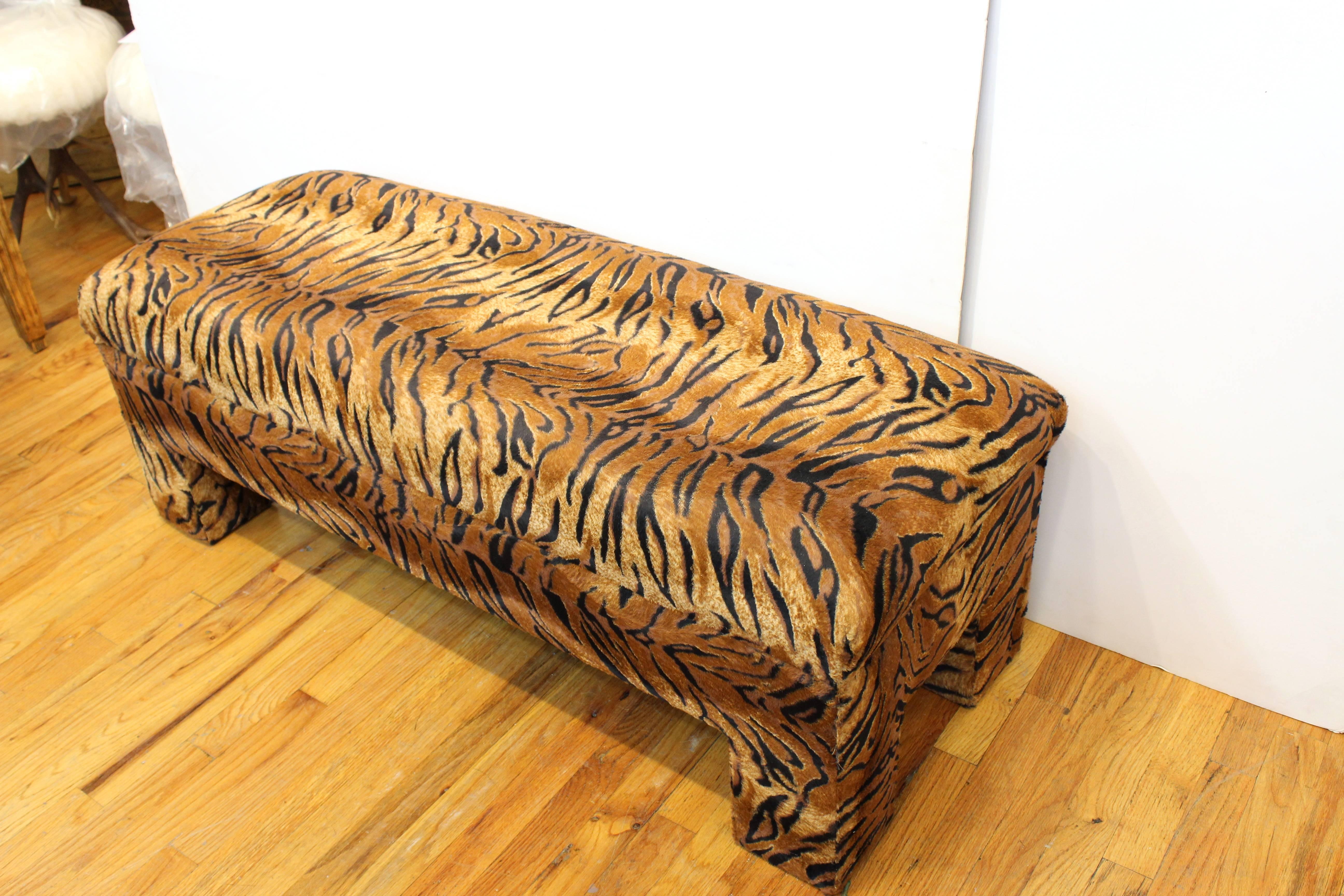 A rectangular shaped bench upholstered in tiger print textile, reminiscent of the opulence of the Hollywood Regency style. The bench can seat up to three people and has recently been re-upholstered. The piece is in good vintage condition with wear