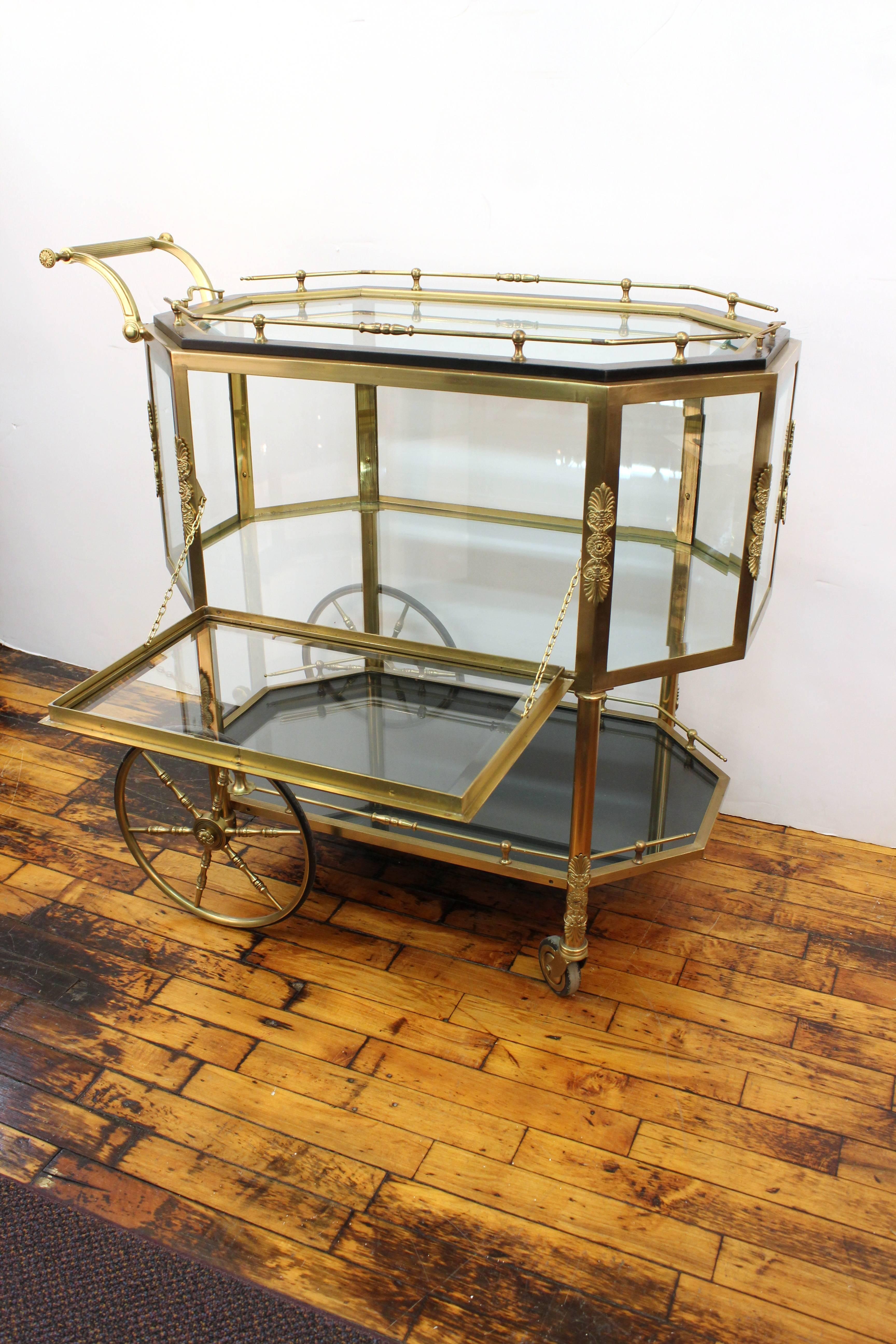 A French brass, glass and wood pastry cart or tea trolley, made in the 1940s in a neoclassical revival style. The trolley has a removable glass tray top and an enclosed shelf for pastries. The upper and lower shelves are gallery-enclosed. Decorative
