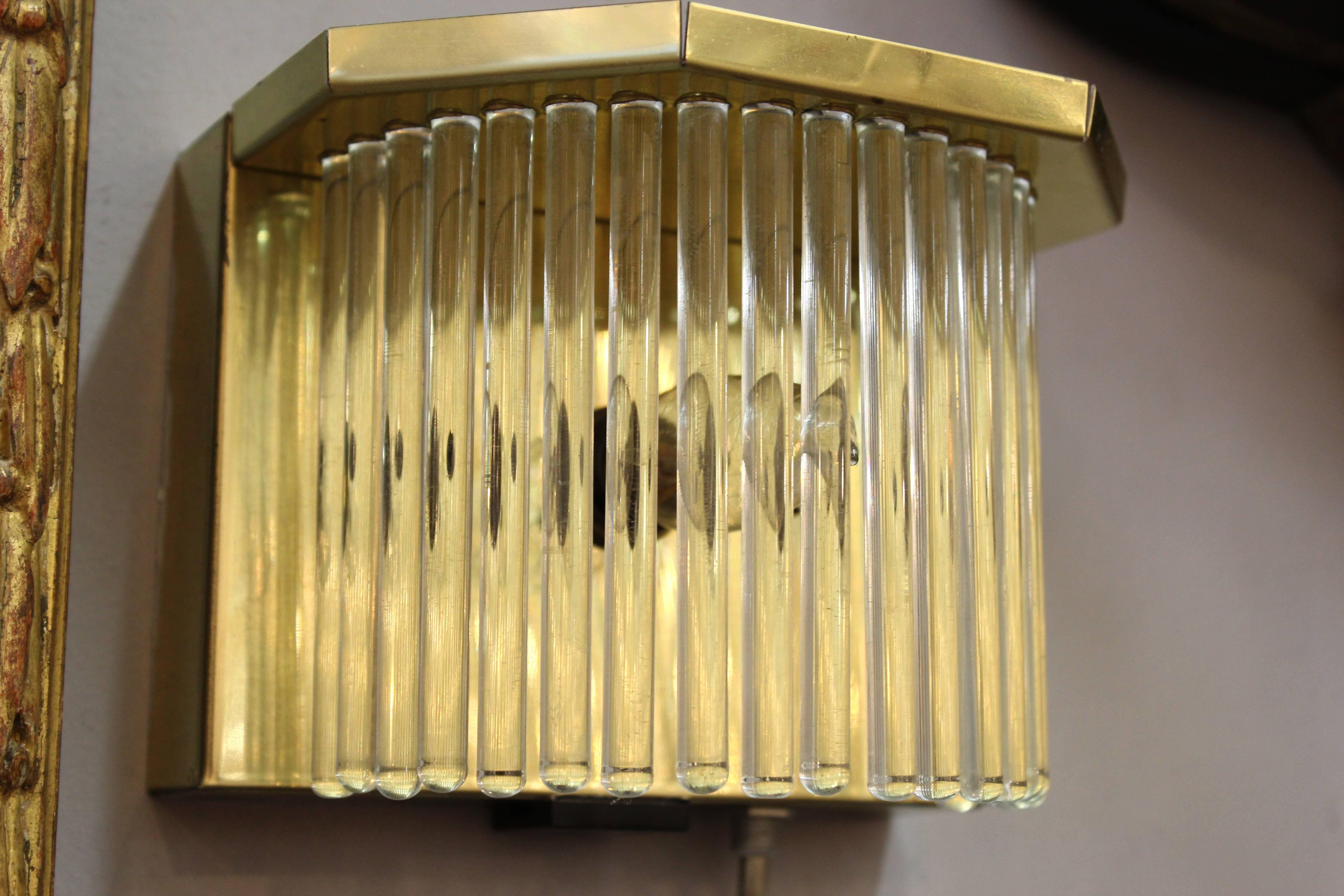 A pair of Mid-Century Modern brass and glass sconces made by designer Gaetano Sciolari in Italy in the 1970s. The brass frame holds a semi-circular row of glass rods that surround the light source. In great vintage condition with age appropriate