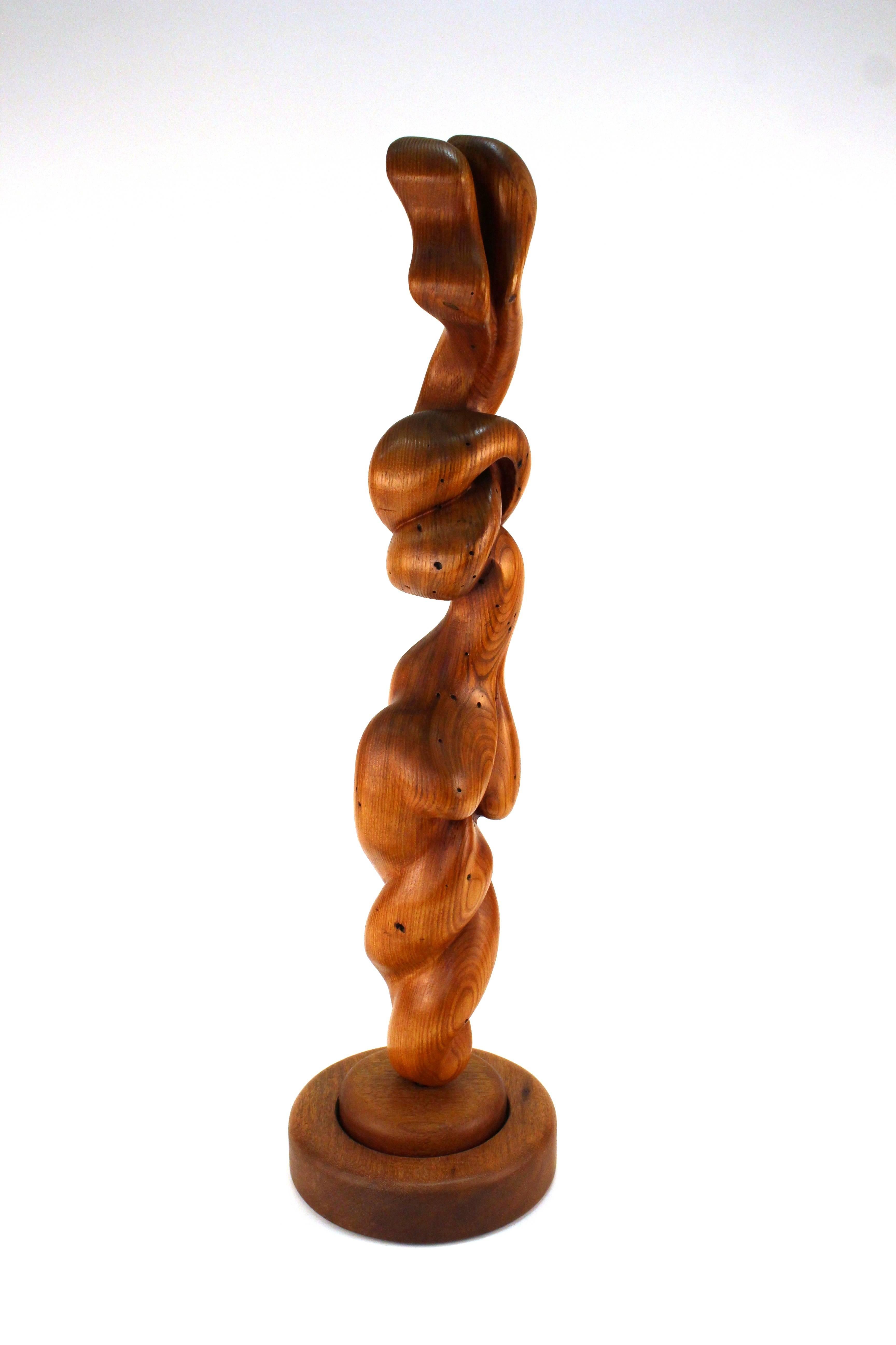 A Biomorphic wooden sculpture in sinuous curves and forms evocative of the human form, on a circular rotating wooden base. The sculpted wood shows its natural grain. Unknown artist's mark on the lower edge where the sculpture meets the base. In