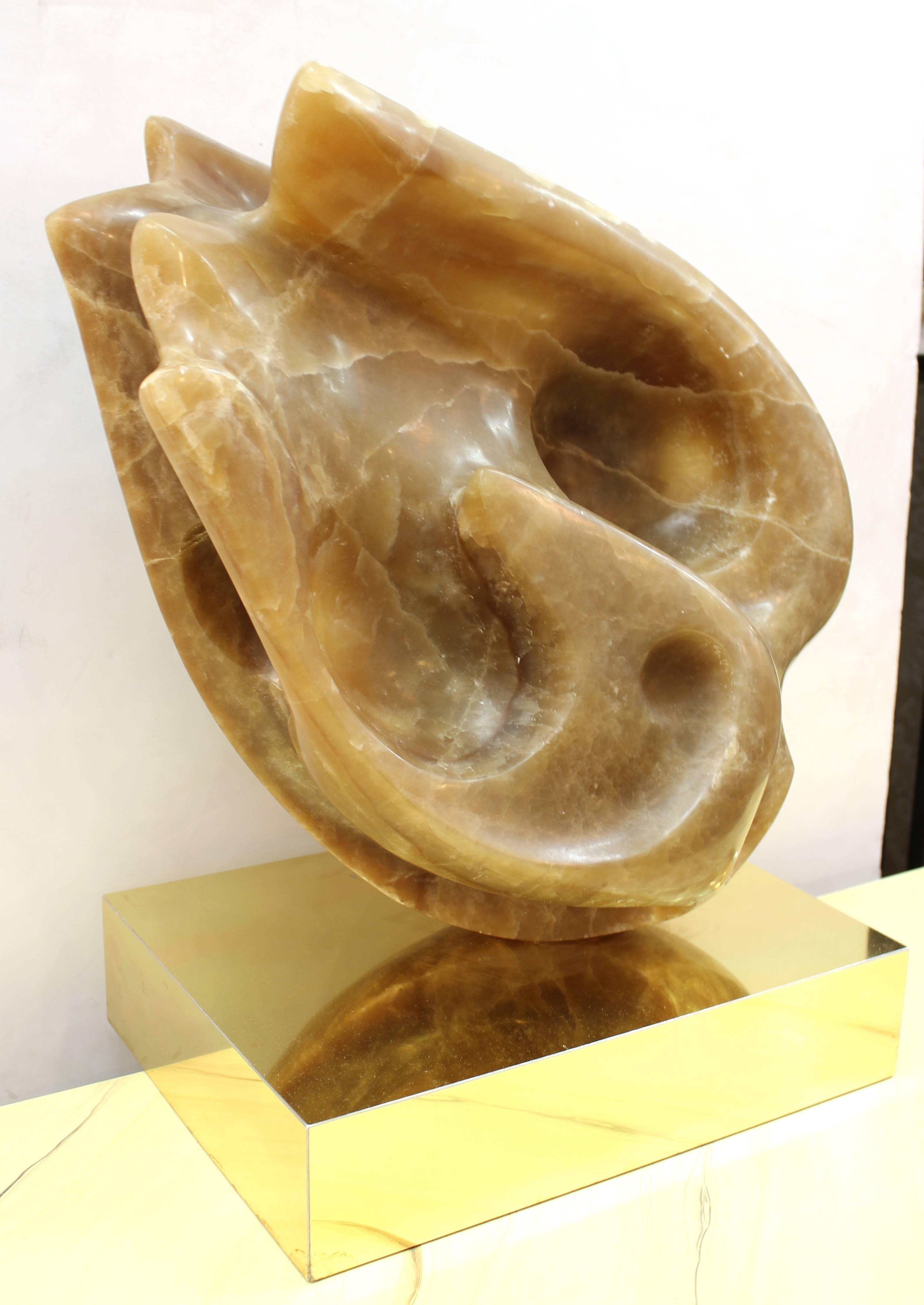 An abstract modernist sculpture carved in onyx, standing atop a base made out of brass. In good vintage condition, with some dents on the edge of the back side of the brass base.