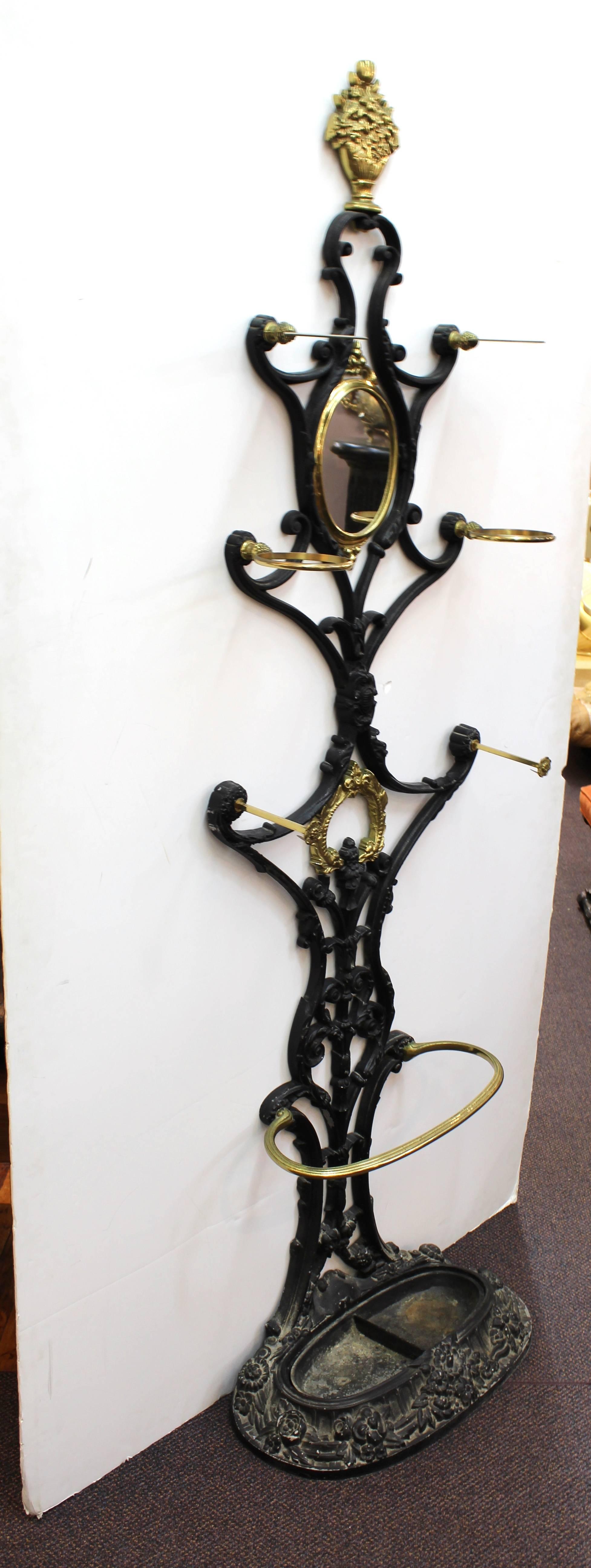 Tall hall tree in black metal with brass details. Includes six hooks in brass and an umbrella stand at the base. Decorated with acanthus leaves, rosettes and a potted bouquet at the top. Wear appropriate to age and use. The hall tree is in good