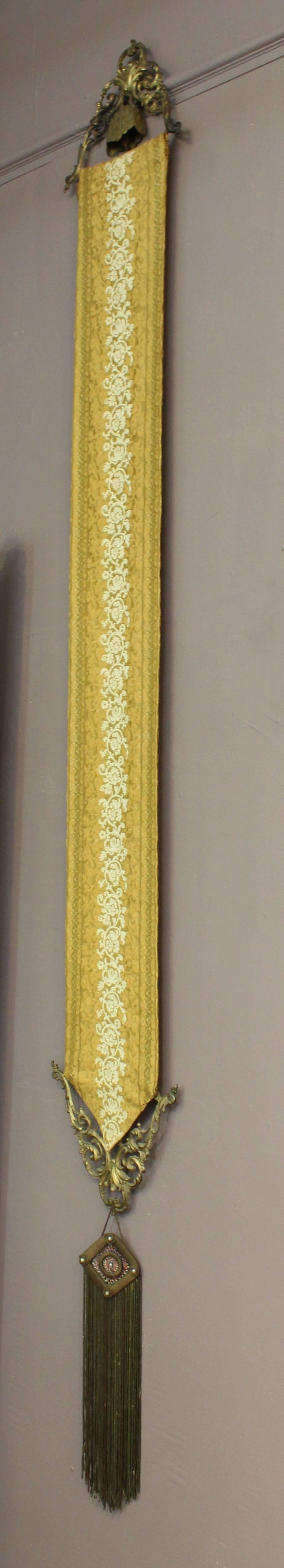 Late nineteenth century brass bell pull with newly upholstered yellow fabric in a scrolling floral pattern. The metalwork at each end is in brass and features a scrolling foliate motif. The bottom of the pull has a decorative woven metallic tassel.