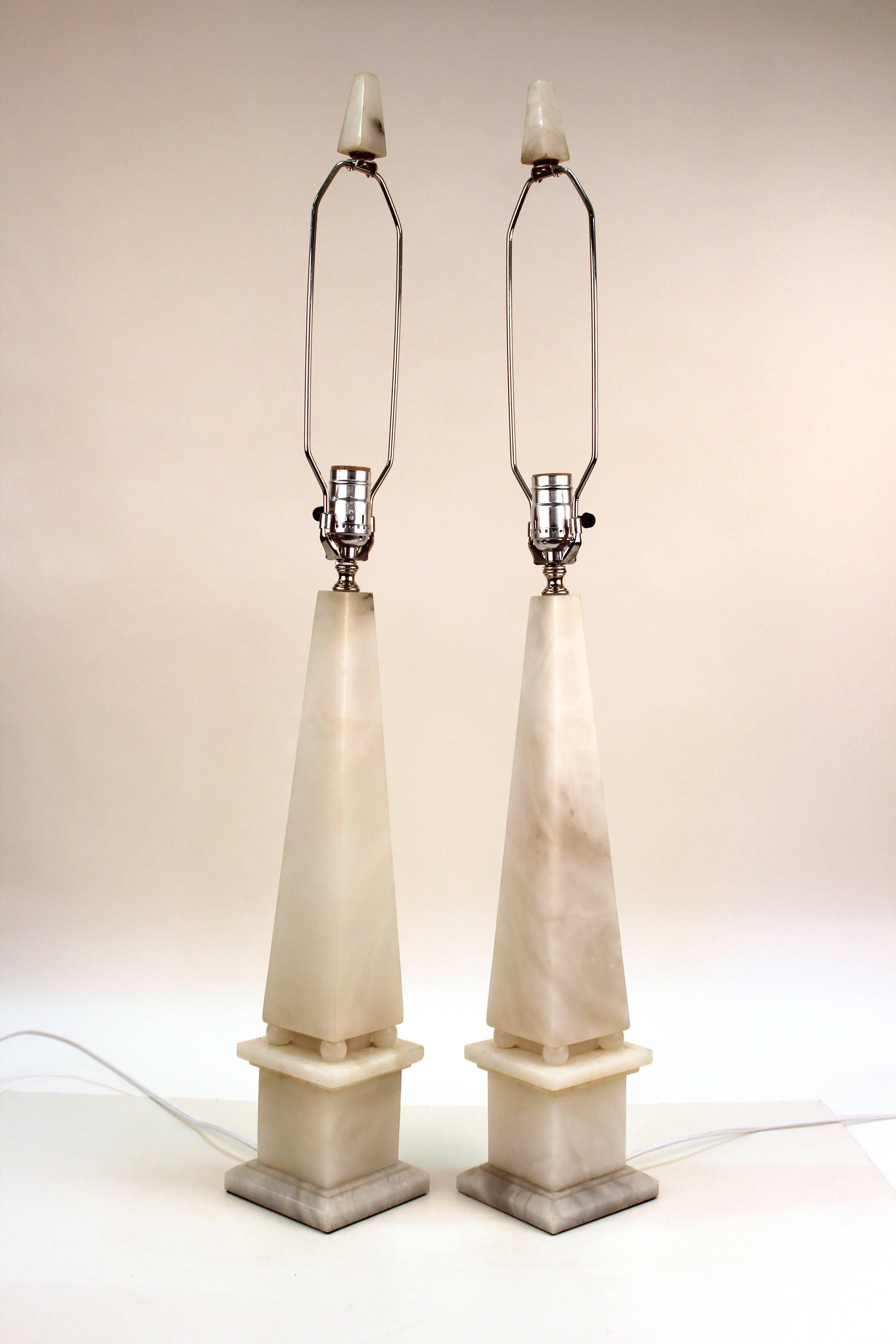 Pair of column lamps in alabaster. Crafted in the form of obelisks with original alabaster finials. Produced in Italy during the Mid-20th Century. The pair are in excellent condition with new silk wiring and sockets. 