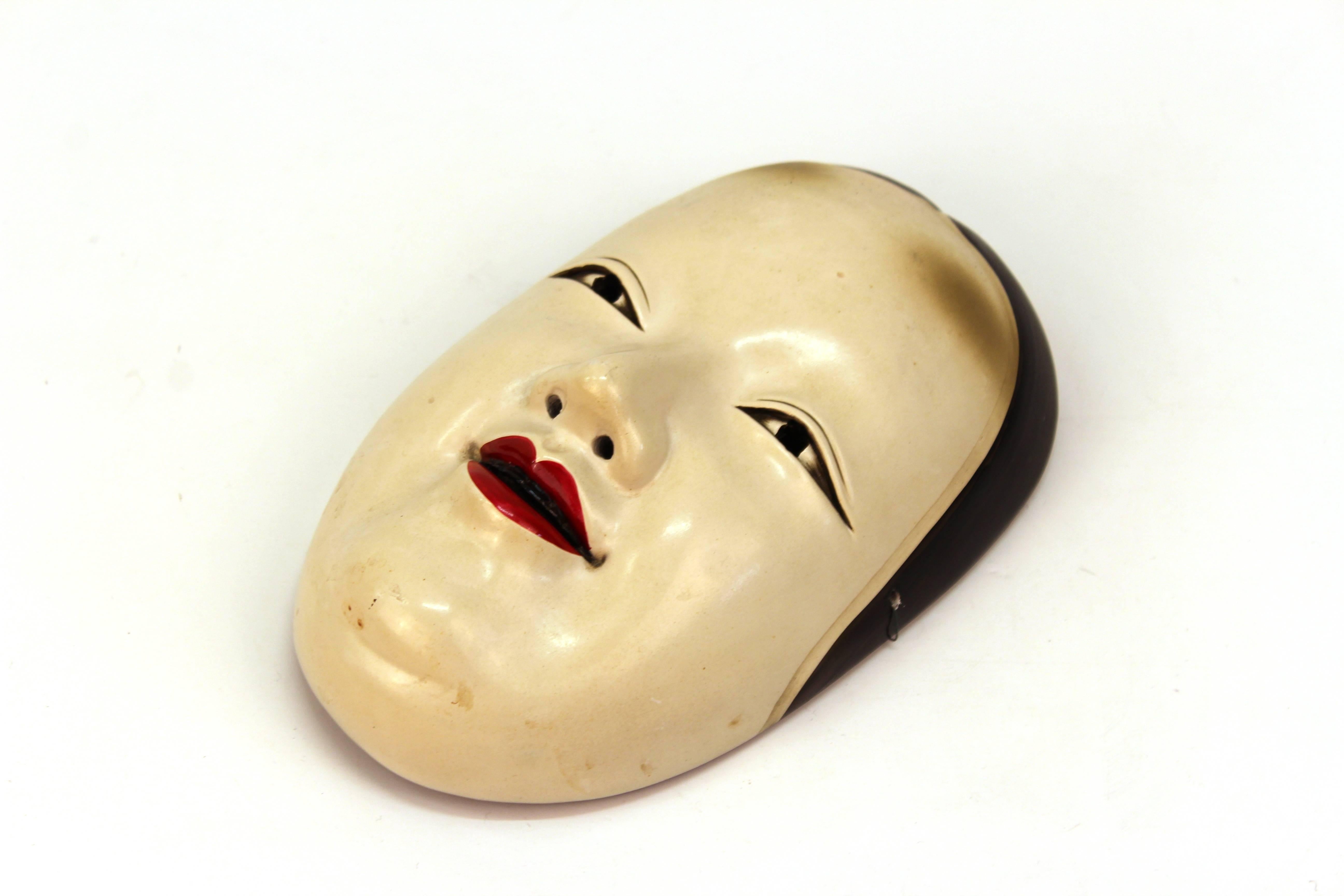 Eine geschnitzte Holzmaske des japanischen Noh-Theaters, die ein junges Mädchen namens Ko-Omote darstellt. Die Maske wurde zu Beginn des 20. Jahrhunderts hergestellt und ist in einem hervorragenden Zustand.
