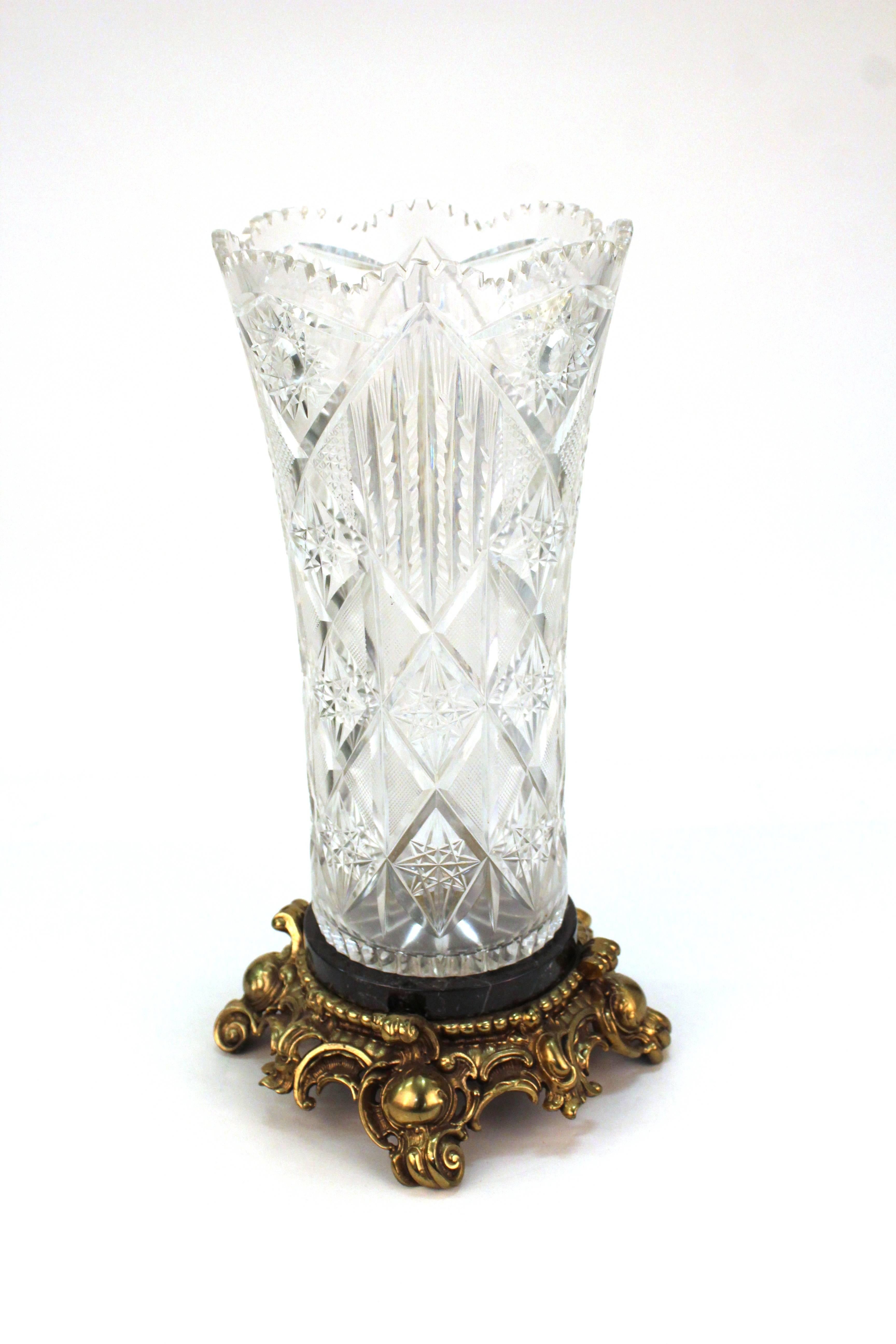 A Victorian era tall cut crystal vase atop a black marble base with elaborately sculpted gilt metal base. The item is in great vintage condition.