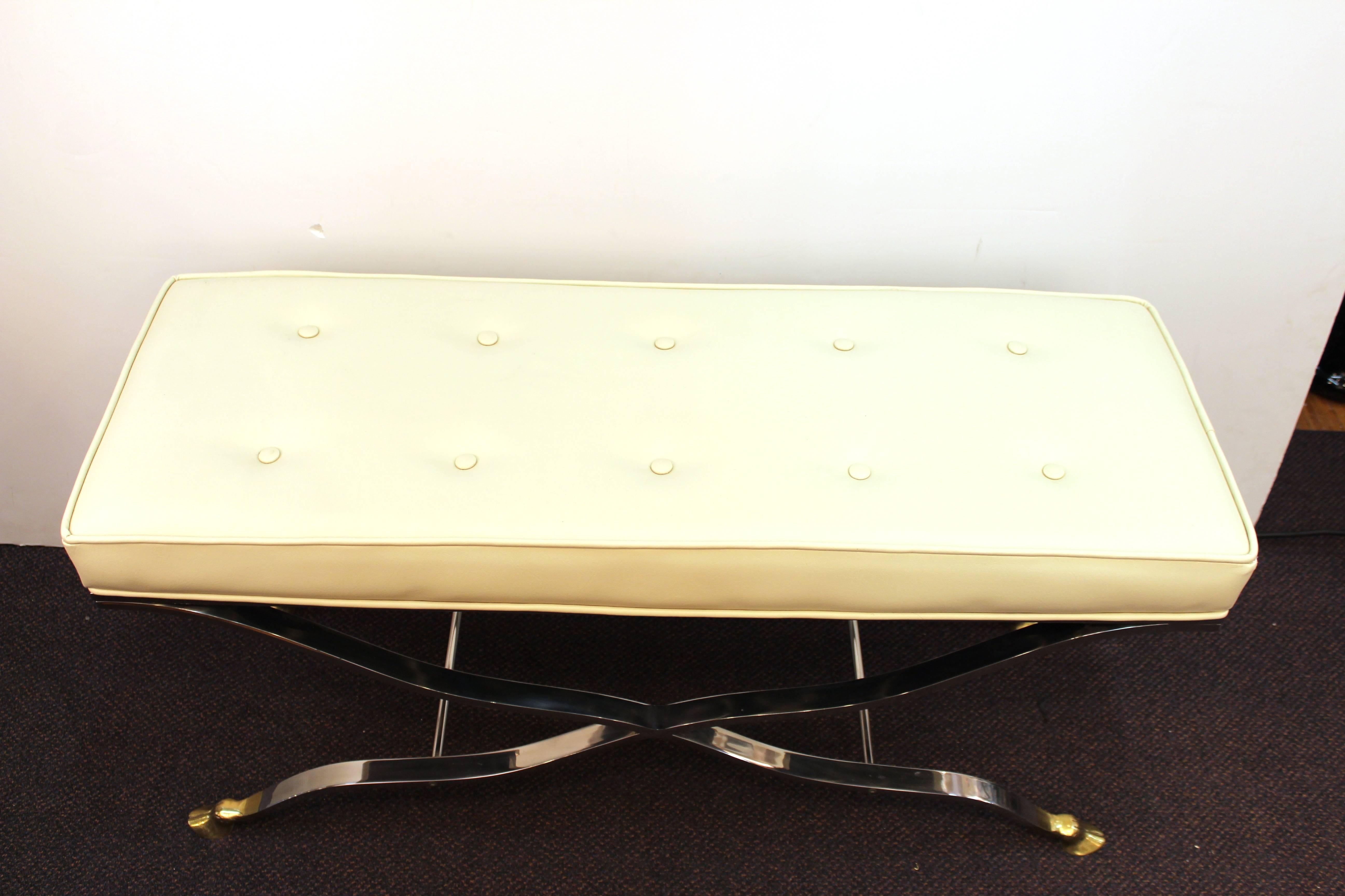 Hollywood regency style bench with cloven feet. Crafted in polished chrome with brass feet. Upholstered in off-white. Wear appropriate to age and use. the bench is in good condition. 