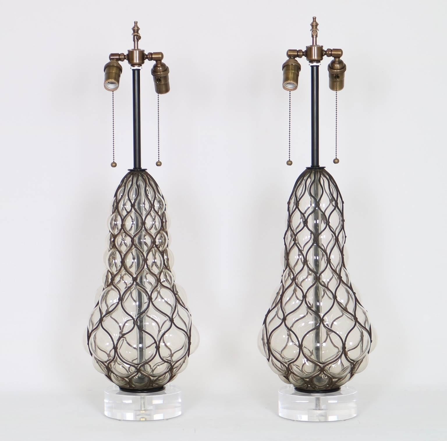 Marbro Hollywood Regency clear Murano glass lamps with iron caging mounted on Lucite bases. Fully restored with all new wiring and hardware including a double socket cluster. In excellent vintage condition having wear consistent with age and