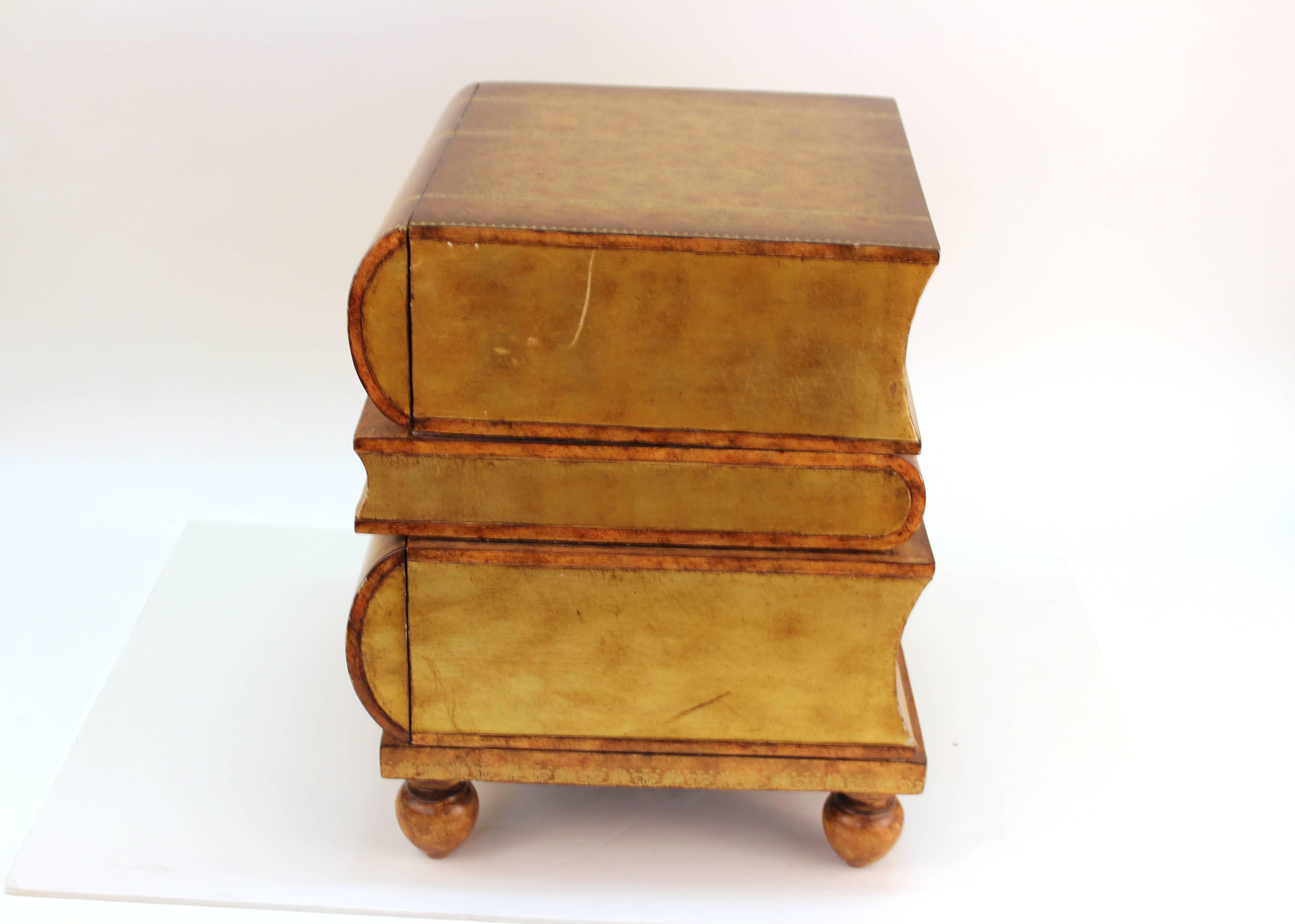 Maitland Smith side table designed to look like a stack of books titled 'The History of Furniture'. Features two hidden drawers and a faux finish to look like leather and paper. The piece stands on four spherical legs. Includes the original logo